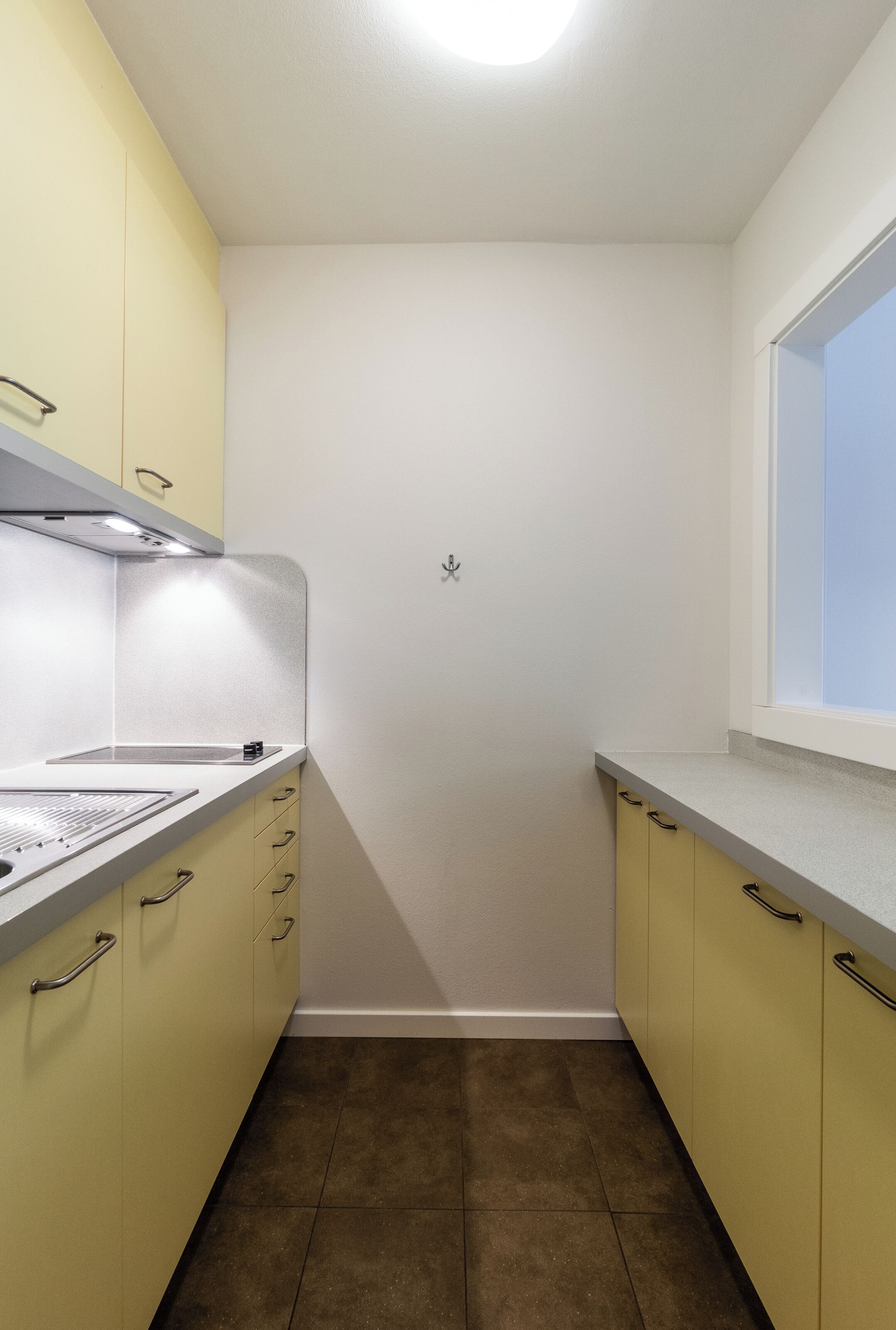 A compact kitchen with yellow cabinets, a white countertop, and a window.
