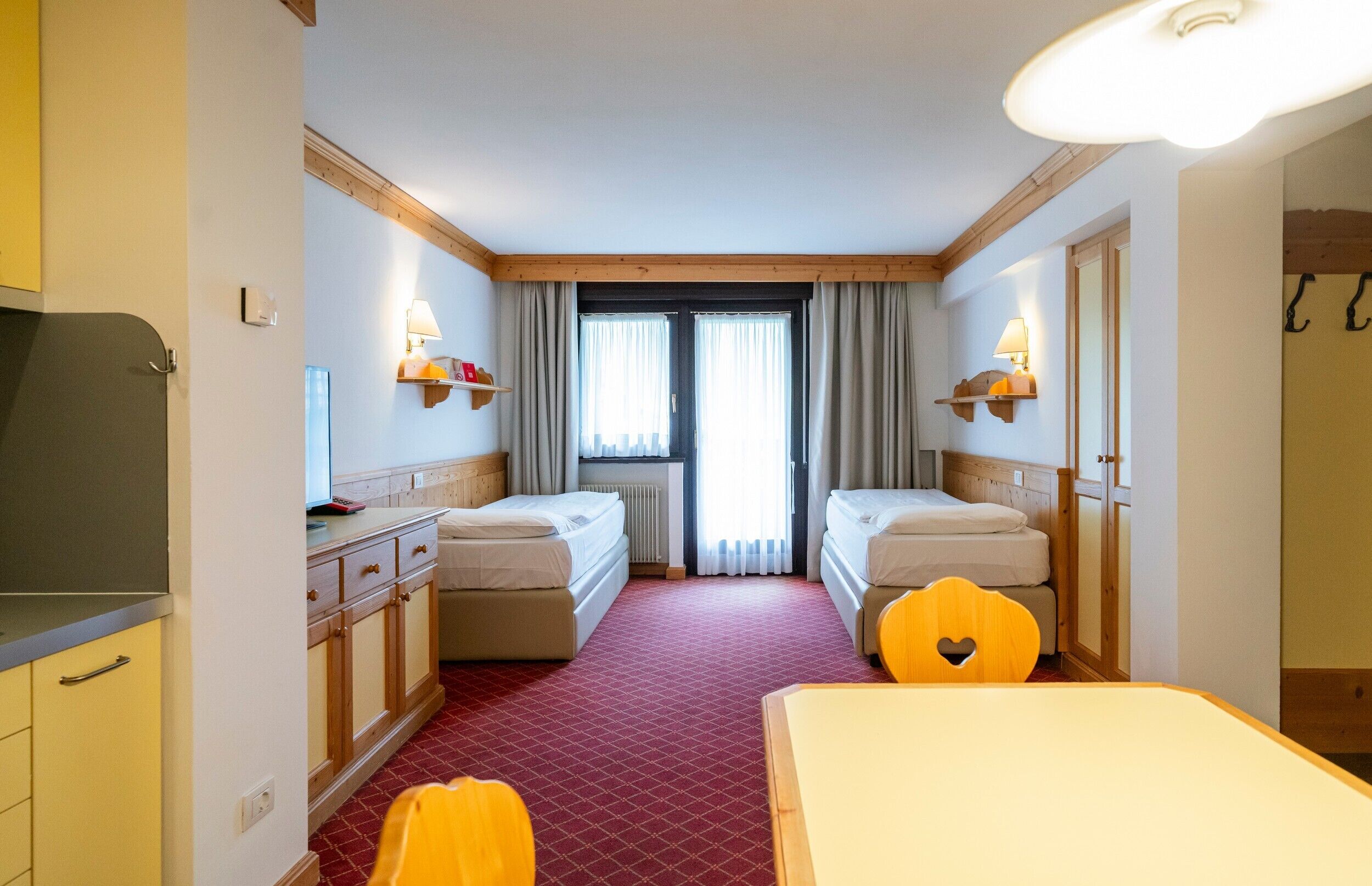 Une chambre d’hôtel avec deux lits, un bureau, une chaise, une télévision et une fenêtre avec des rideaux.
