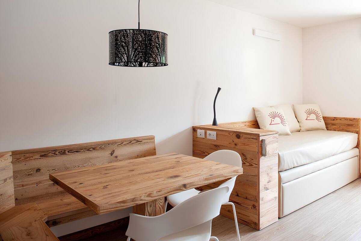 A compact room with a wooden dining table and bench, a white sofa with decorative pillows, and a hanging pendant light.