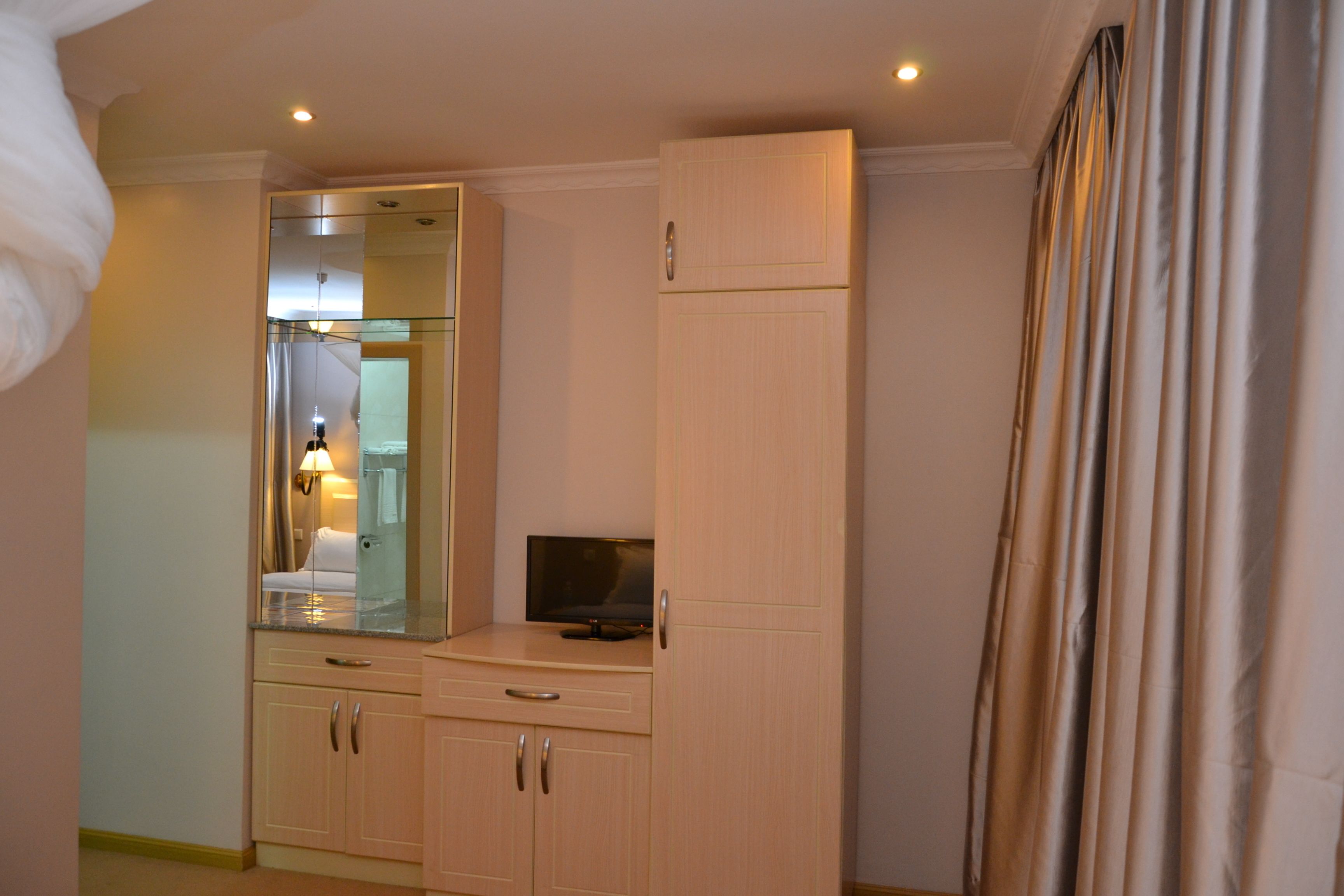 A hotel room with a large mirror, a flat-screen TV, and a wardrobe.