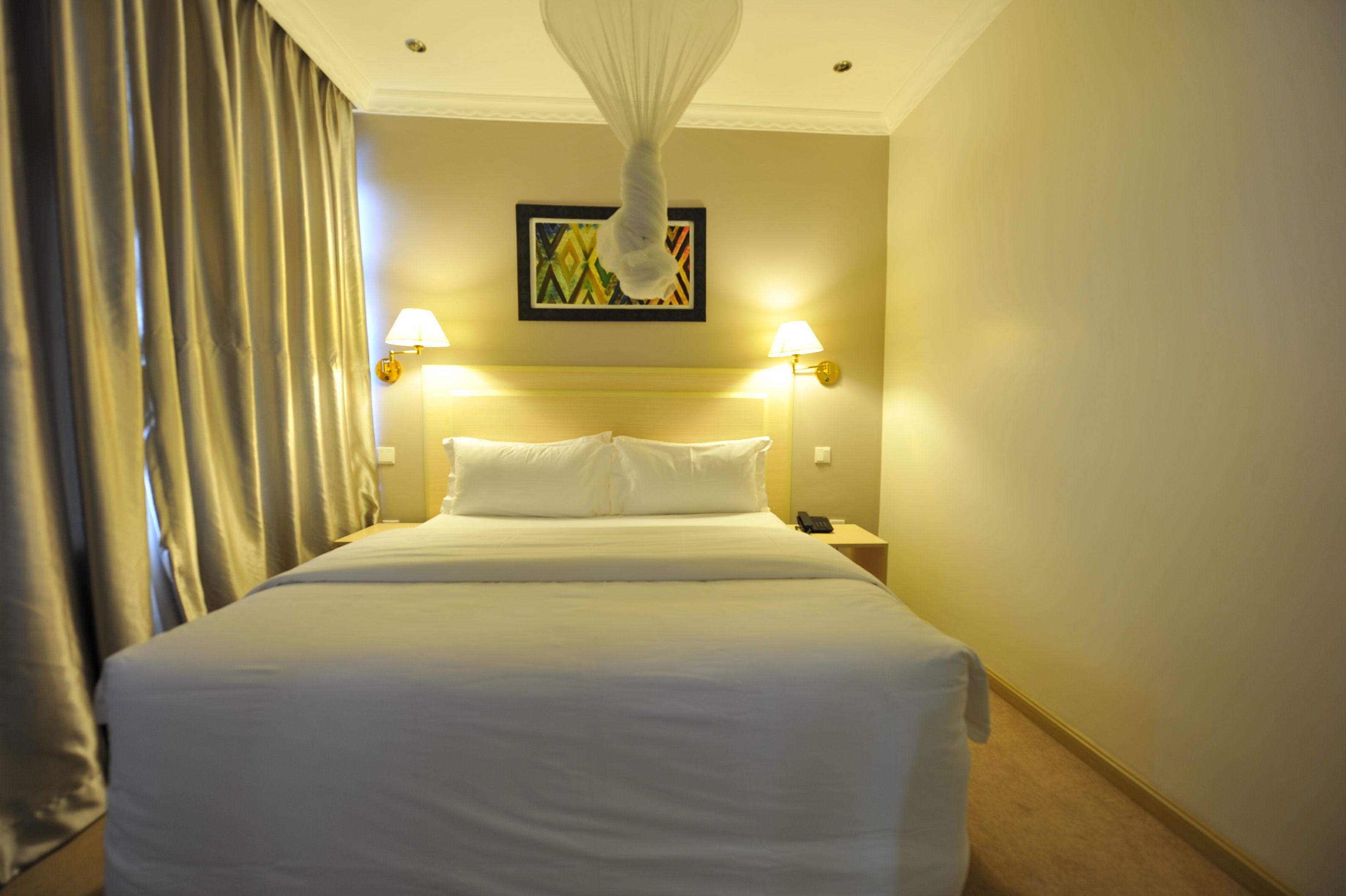 Una camera d'albergo con un letto grande, due lampade sui comodini, un telefono e un lampadario.