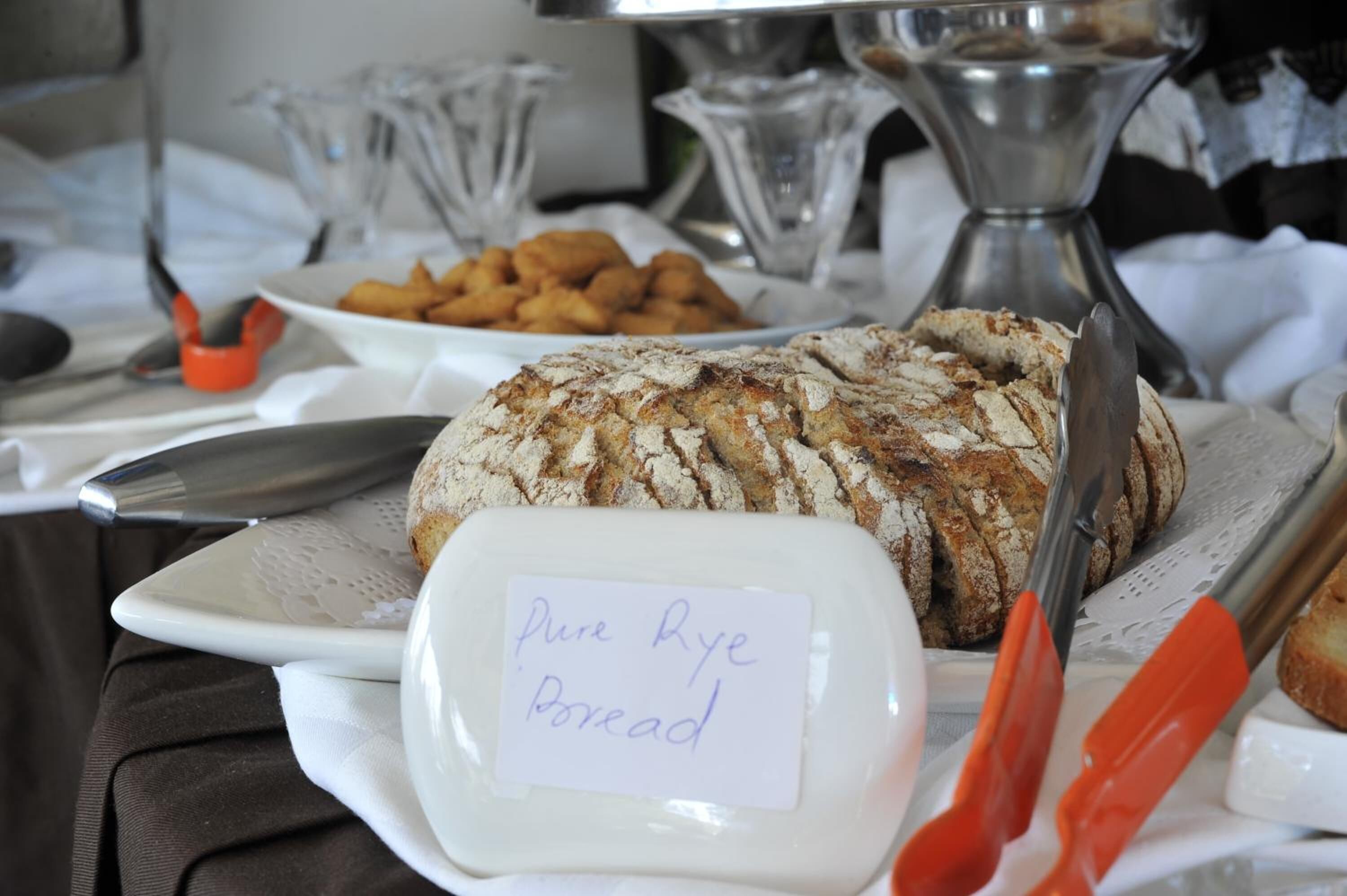 A table with a loaf of rye bread, a plate labeled "Pure Rye Bread," and a bowl of pretzels.