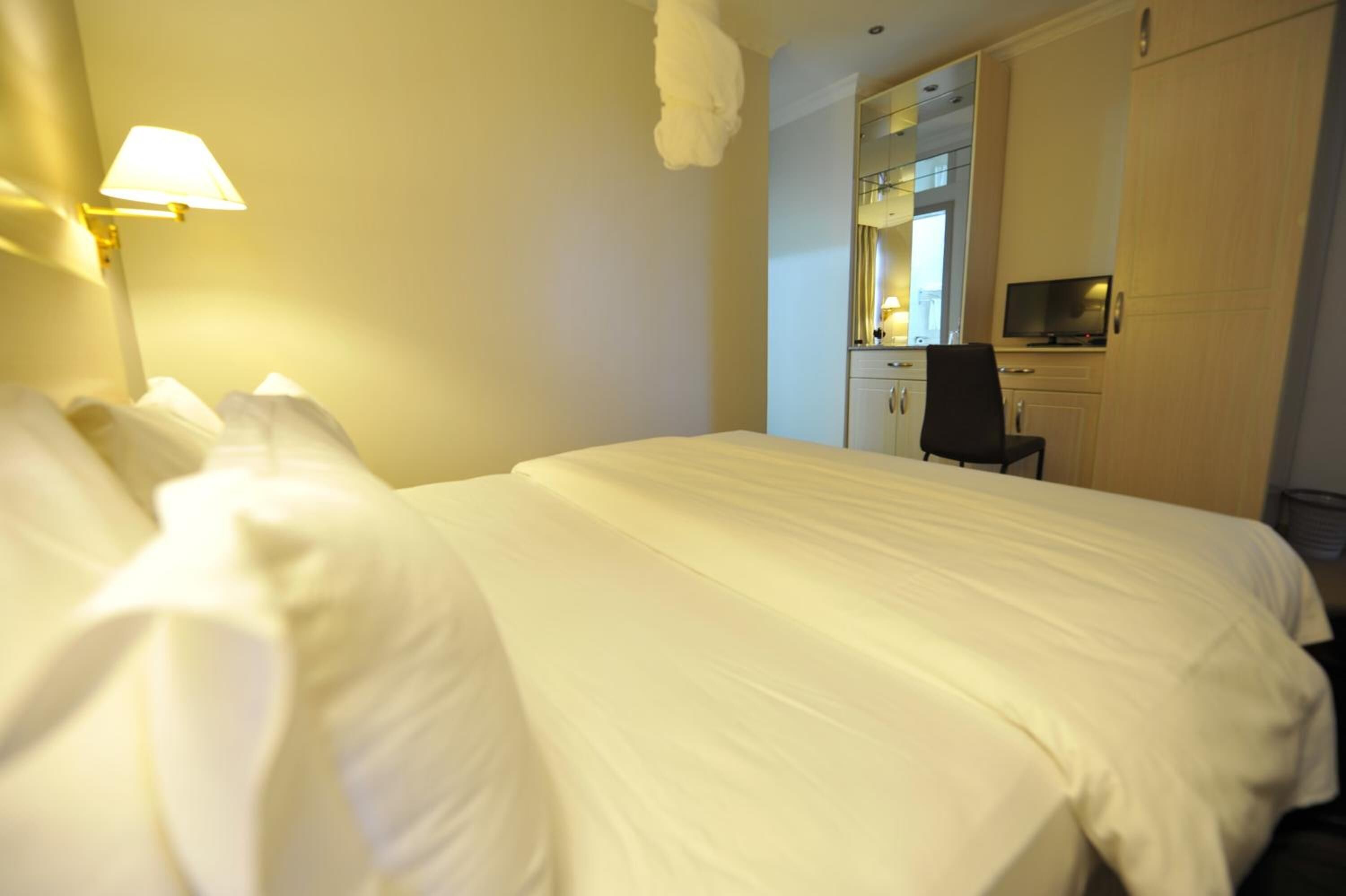 Una habitación de hotel con una cama bien hecha, un escritorio con silla, un televisor y un espejo.