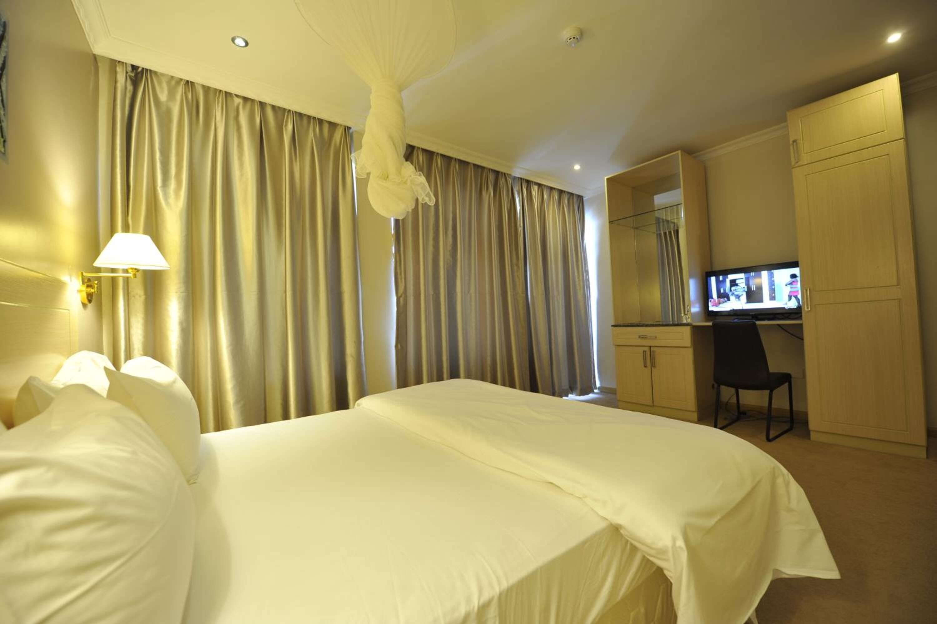 A hotel room with a large bed, a desk, a chair, and a television.