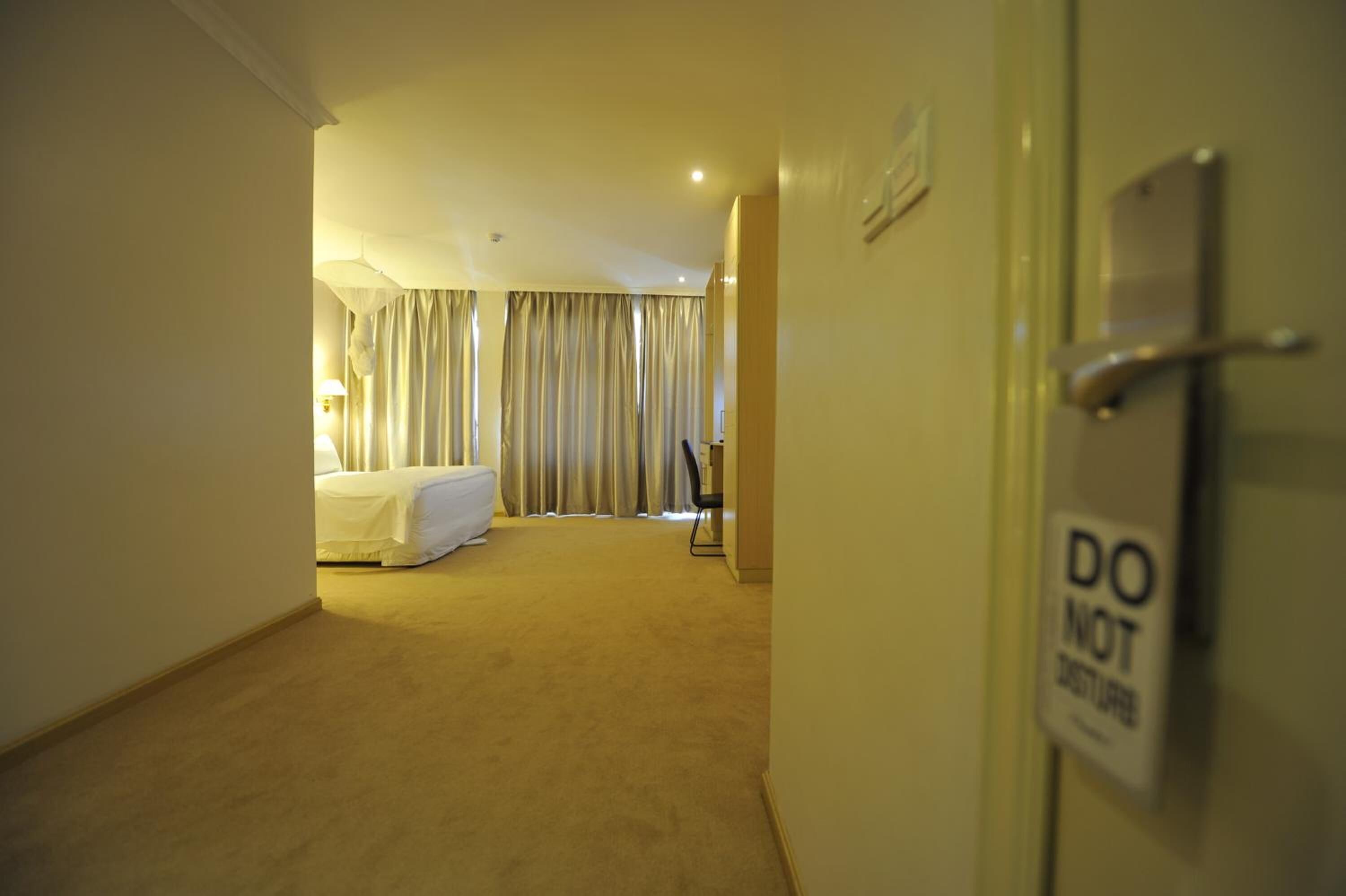 A hotel room with a bed, curtains, a desk, and a 'DO NOT DISTURB' sign.