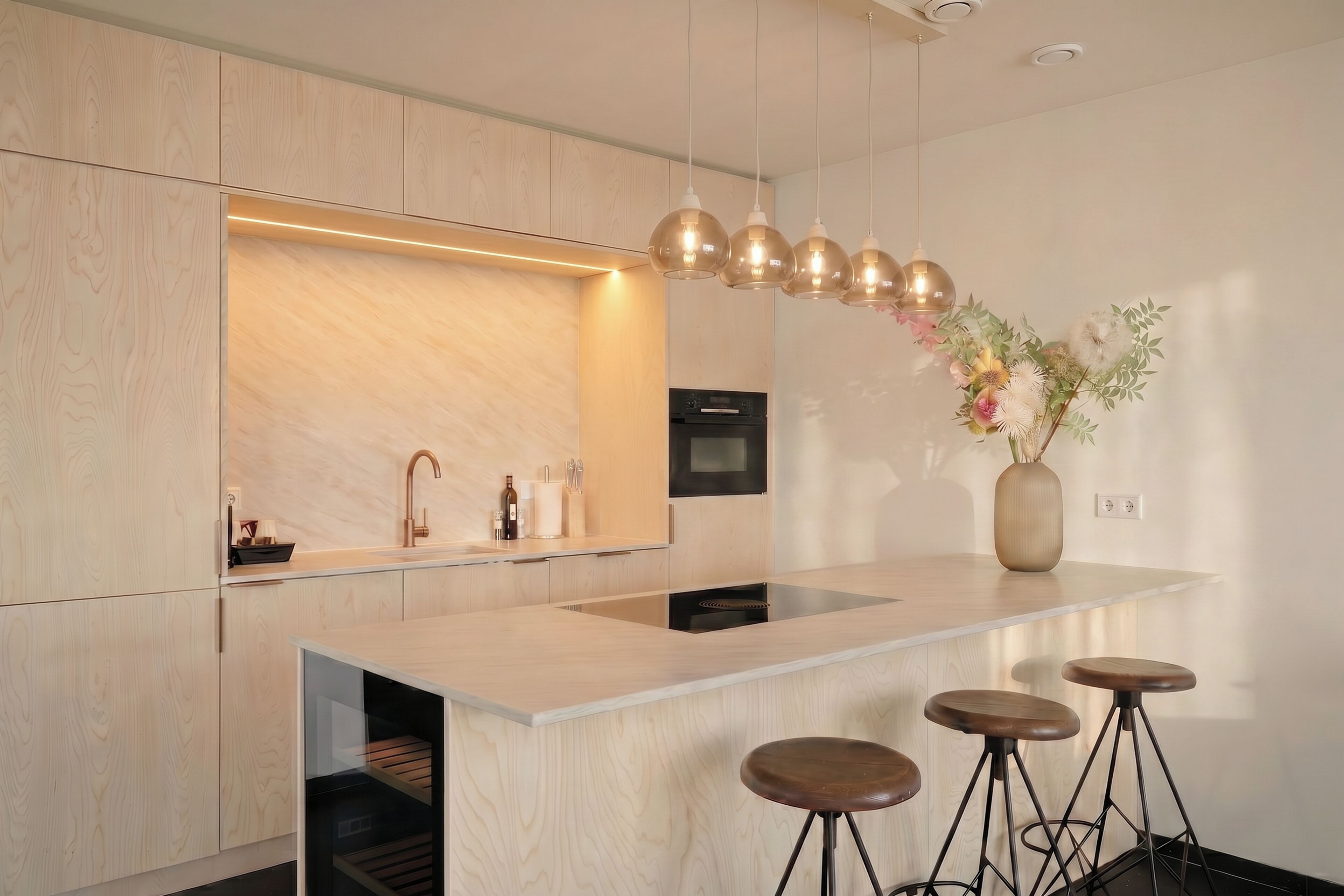 A modern kitchen with a central island, bar stools, pendant lighting, and a vase with flowers.