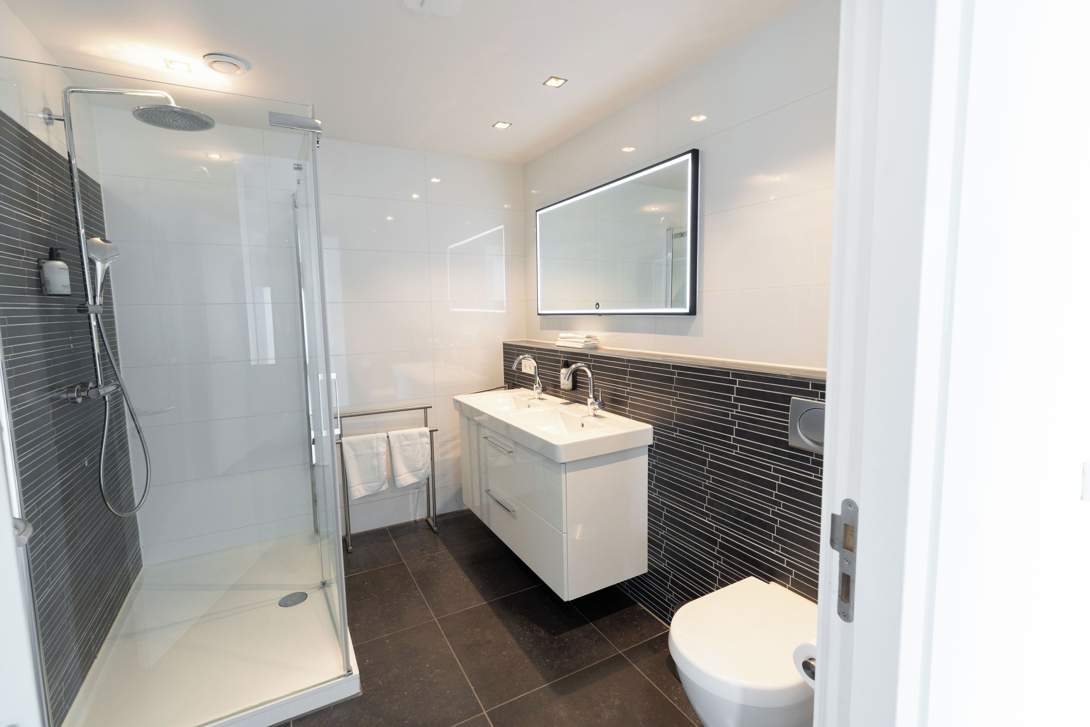 A modern bathroom with a glass-enclosed shower, a white sink, and a large mirror.