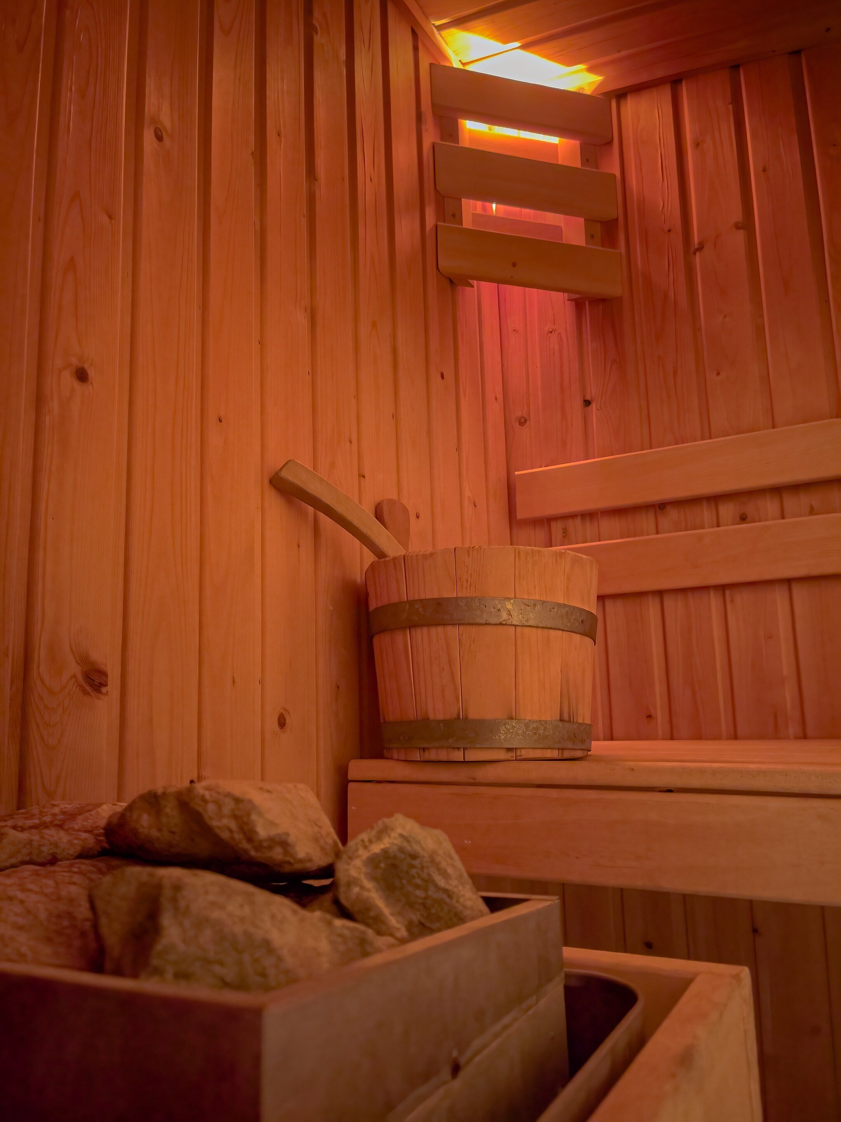 A wooden sauna with a bench, a bucket, and a stone-filled container.