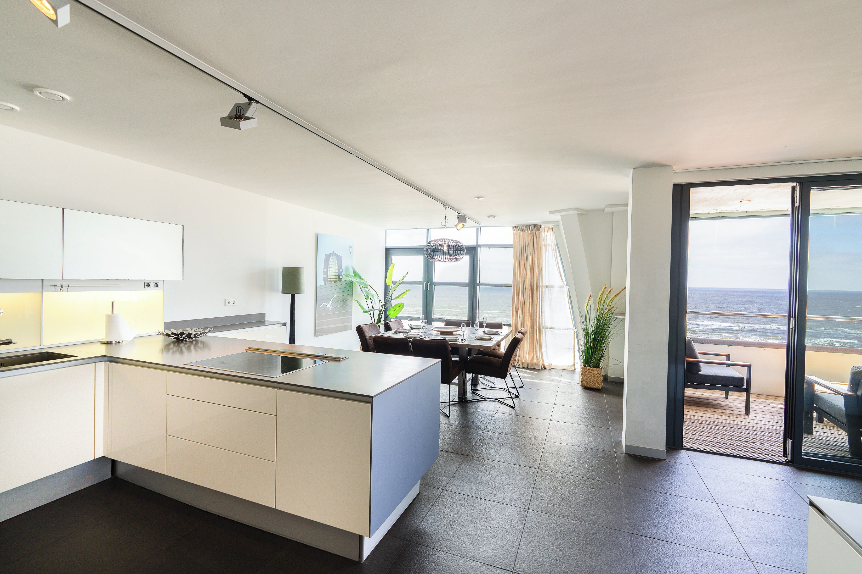 Une cuisine moderne dotée d’un îlot central, un coin repas offrant une vue sur l’océan et un balcon avec vue sur la mer.