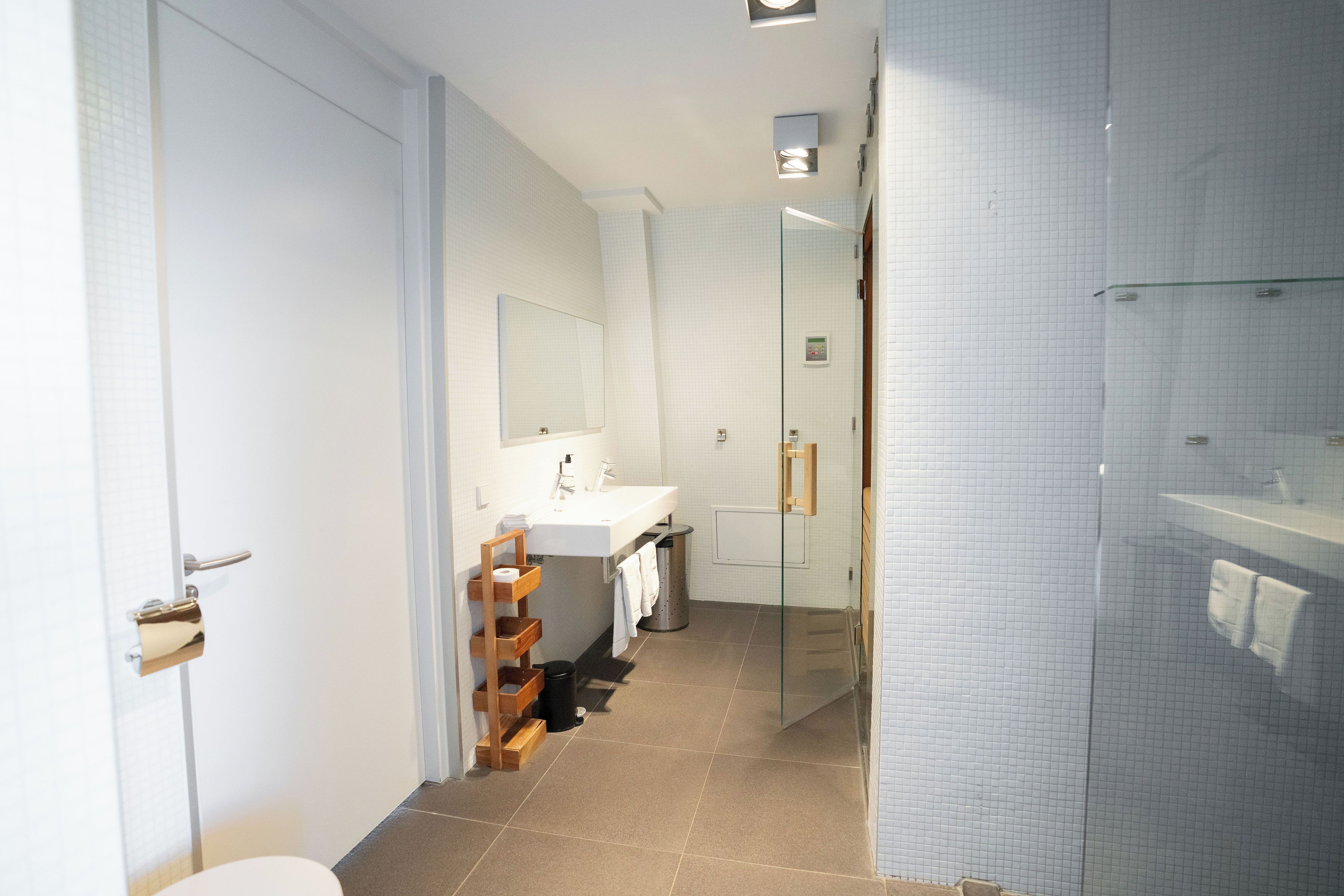 Ein modernes Badezimmer mit Duschabtrennung aus Glas, einem weißen Waschbecken und einem hölzernen Handtuchhalter.