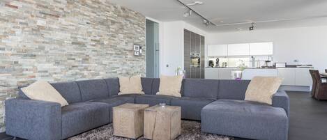 A modern living room with a gray sectional sofa, two wooden side tables, a shaggy rug, and a stone-patterned wall.