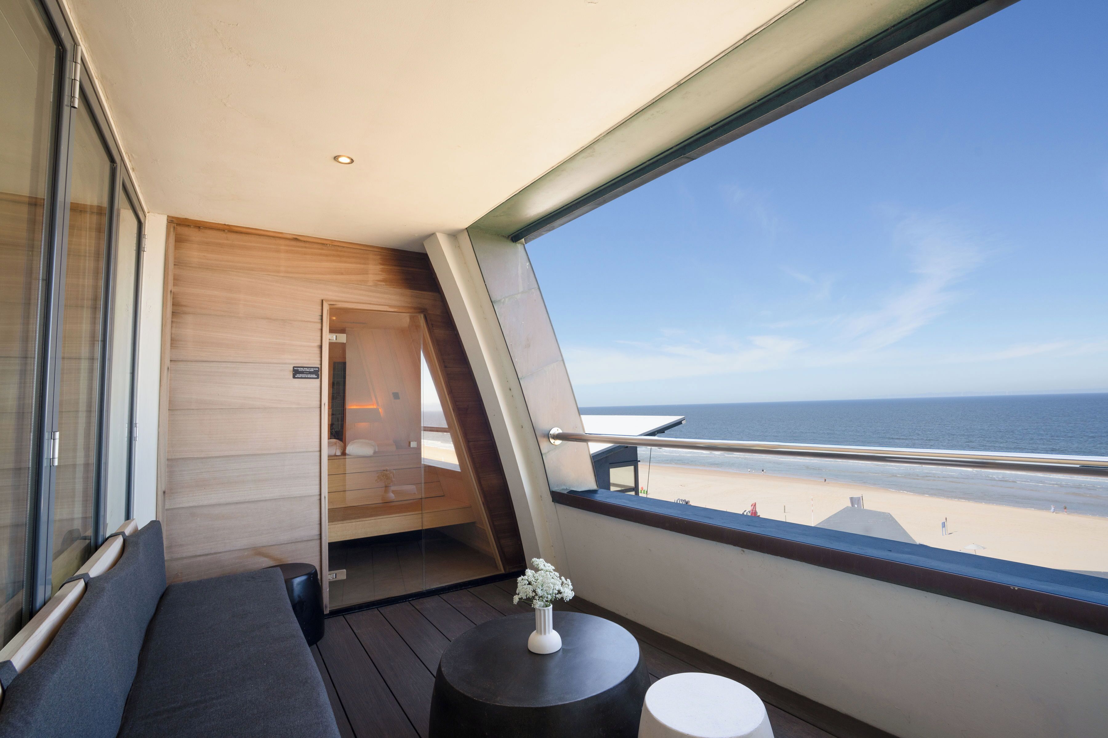 A balcony with a view of the beach, a seating area with a small table, and a wooden door.
