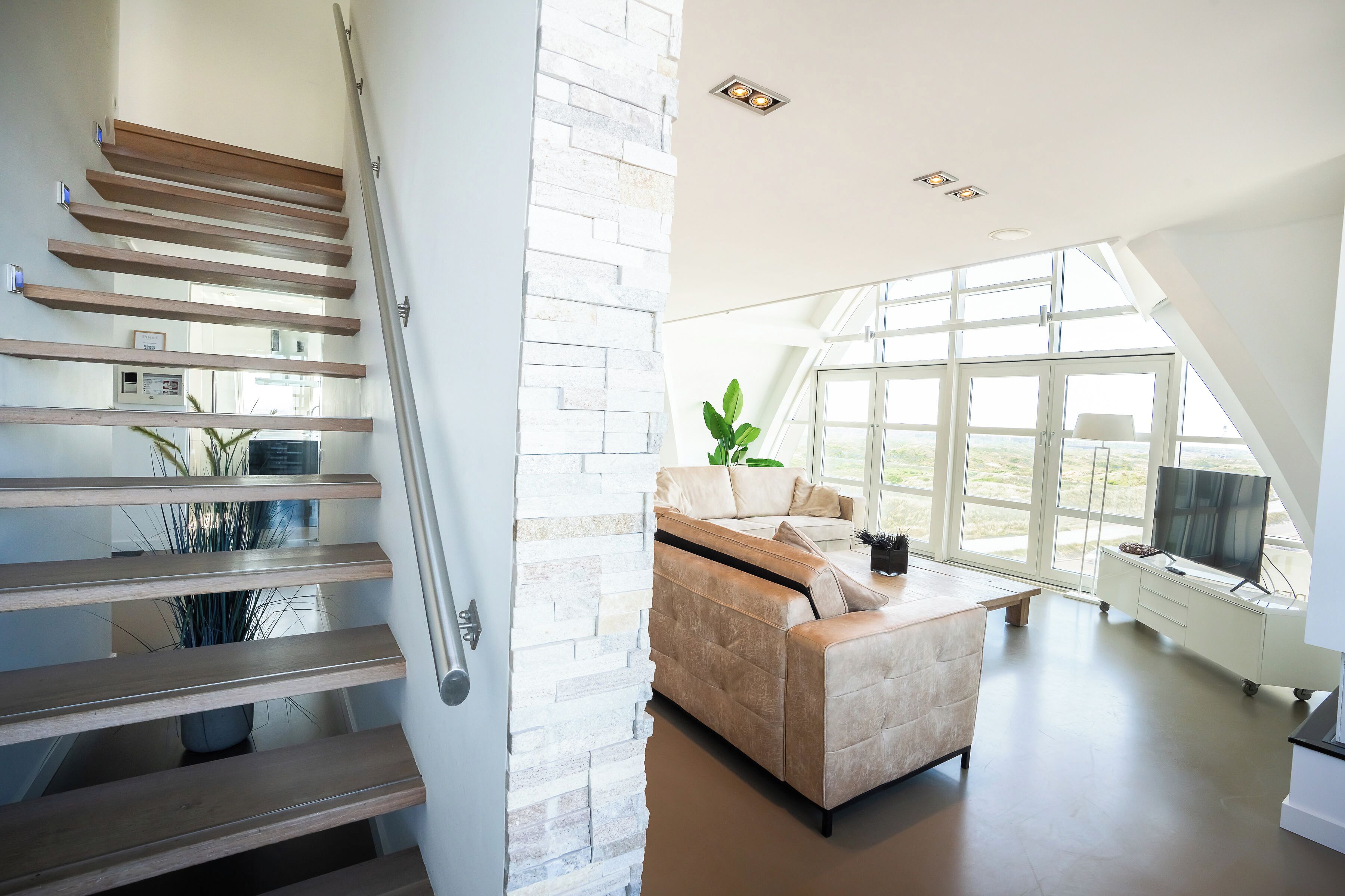 A modern interior with a staircase, a sofa, and large windows.