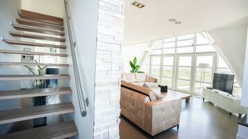 A modern interior with a staircase, a sofa, and large windows.