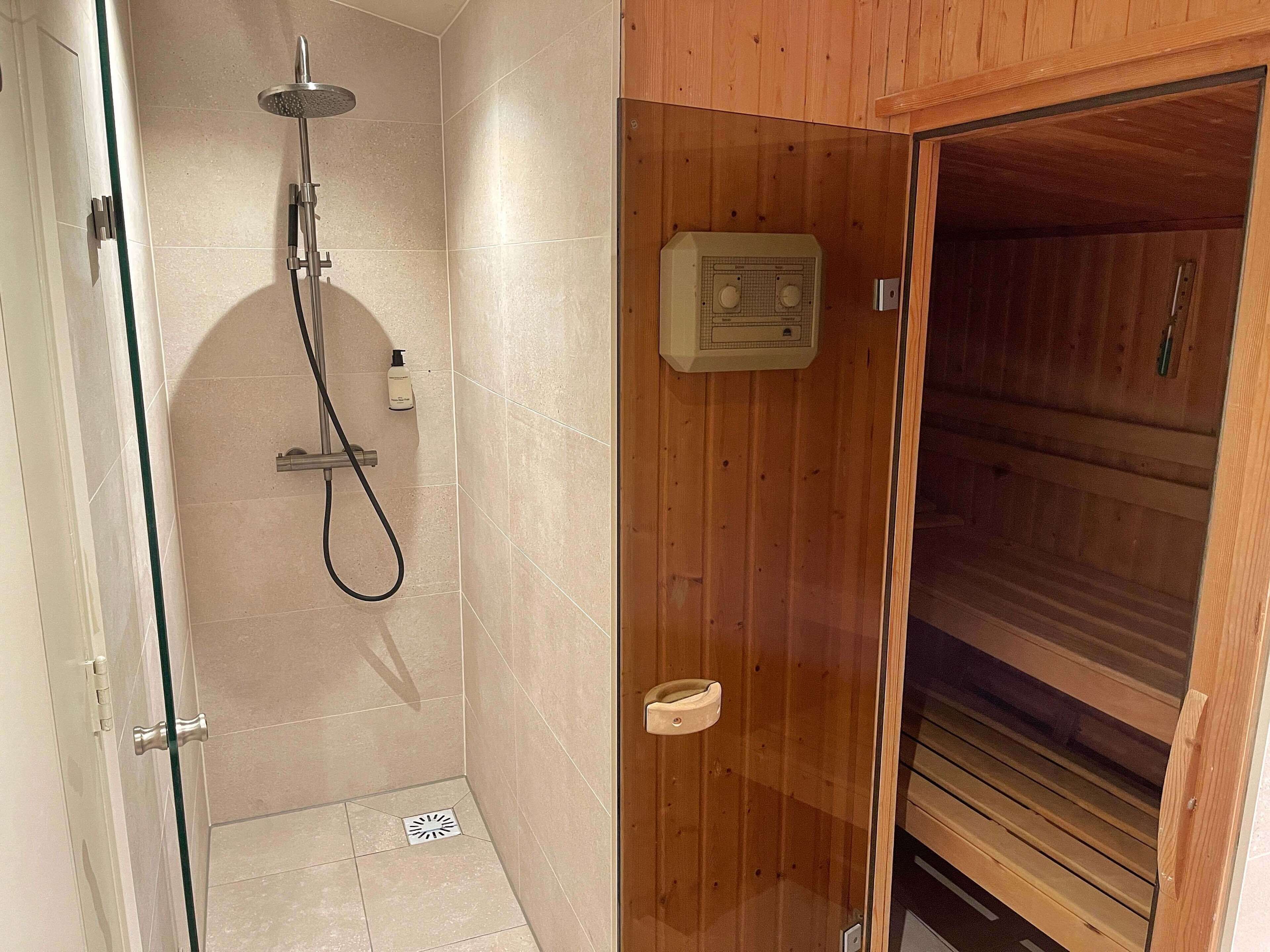 Douchegedeelte met douchekop en handdouche, plus een zeepdispenser aan de wand.
