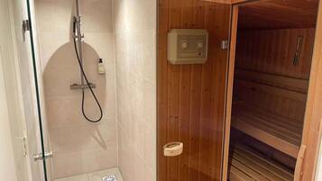 Douchegedeelte met douchekop en handdouche, plus een zeepdispenser aan de wand.