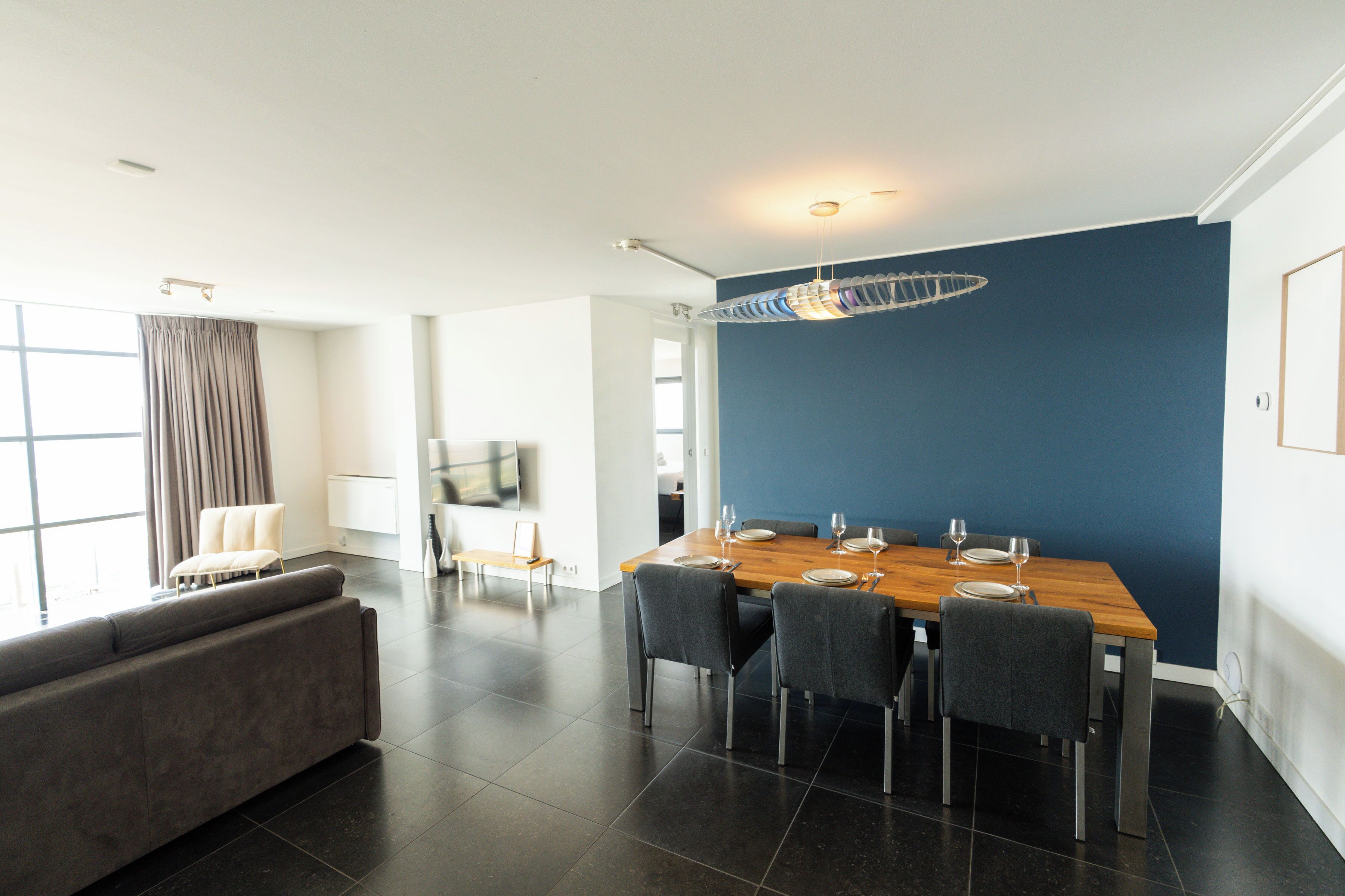 A modern dining area with a wooden table, four chairs, and a blue accent wall.