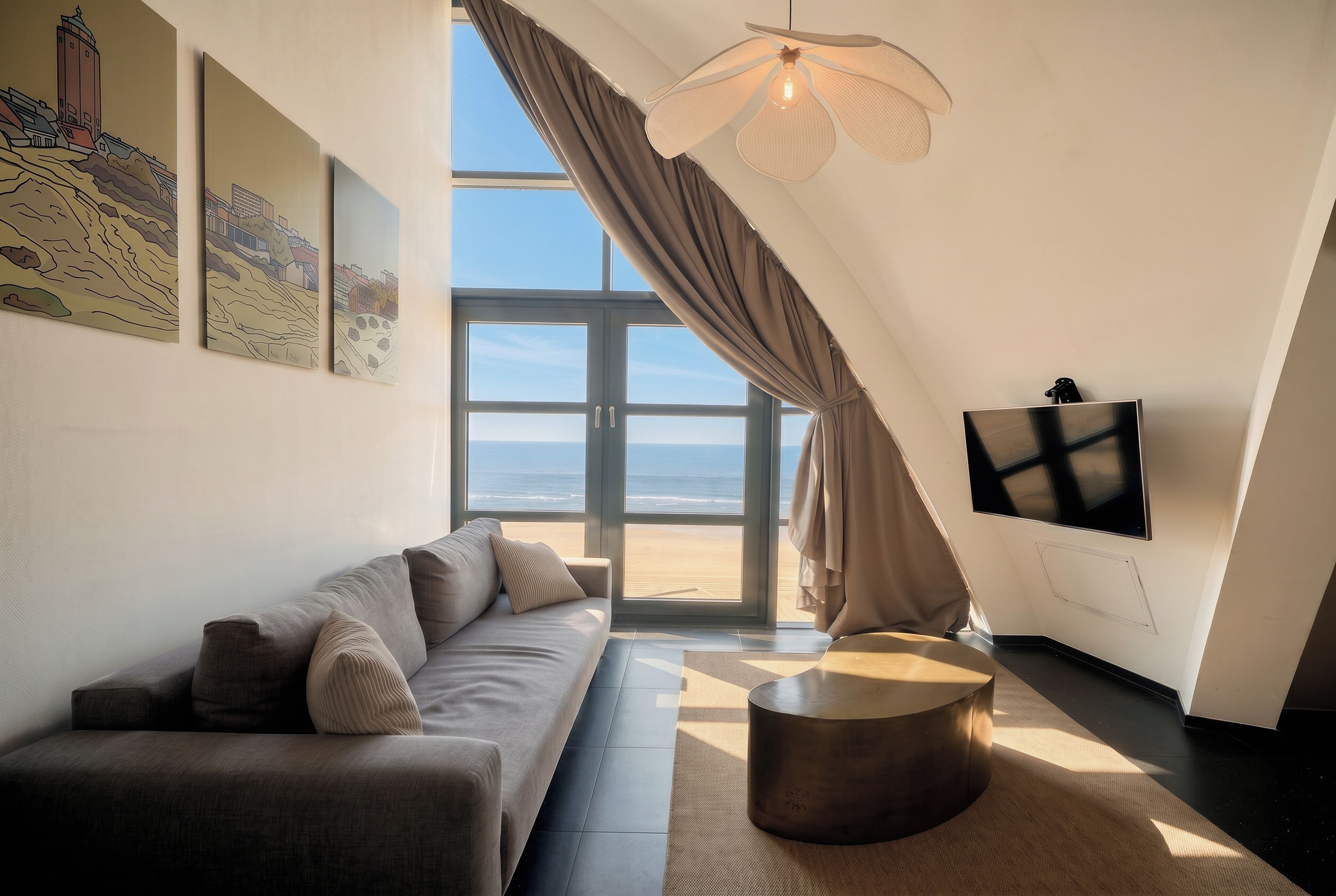 Ein modernes Wohnzimmer mit einer Couch, einem Couchtisch, einem Flachbildfernseher und einem großen Fenster mit Blick auf den Strand.