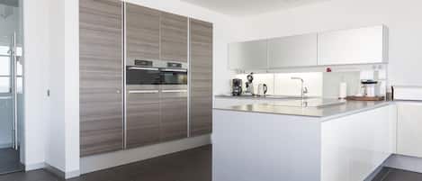 A modern kitchen with a central island, built-in appliances, and a large window.