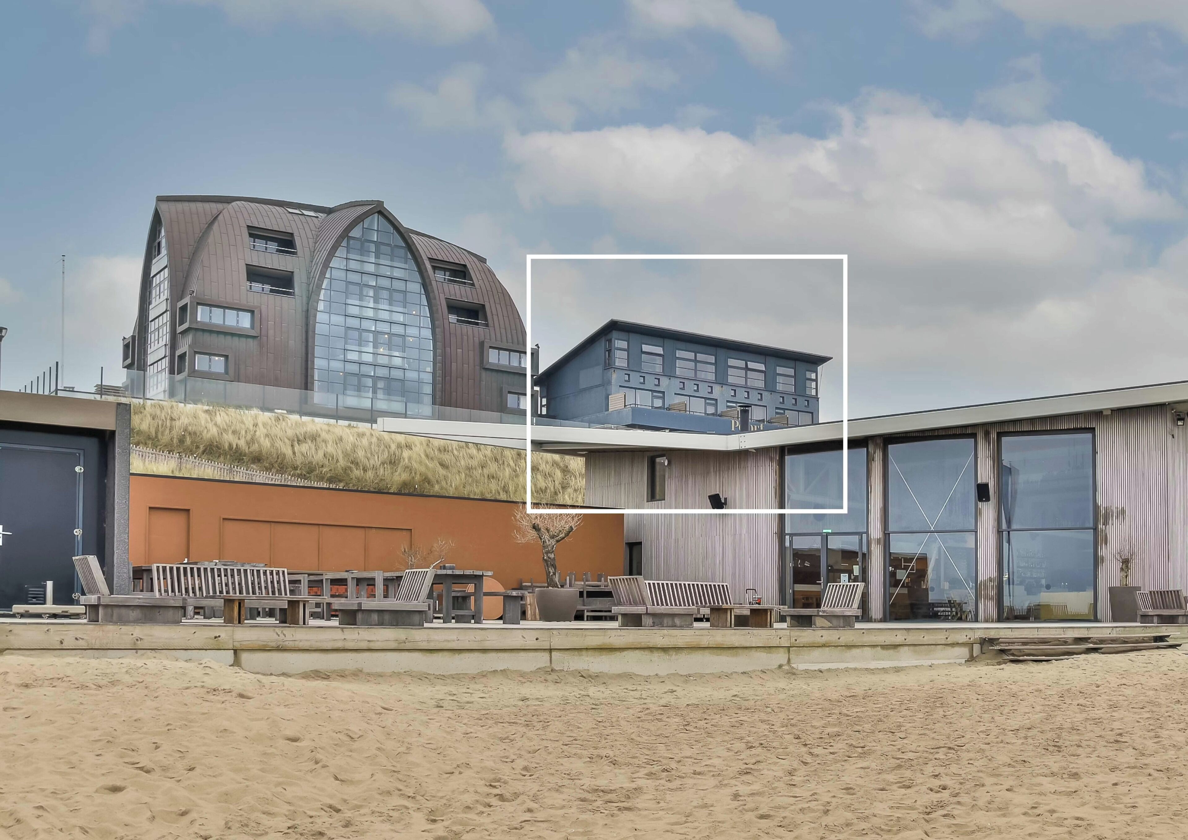 A modern building with a unique curved roof, large windows, and a flat roof section with a blue facade.