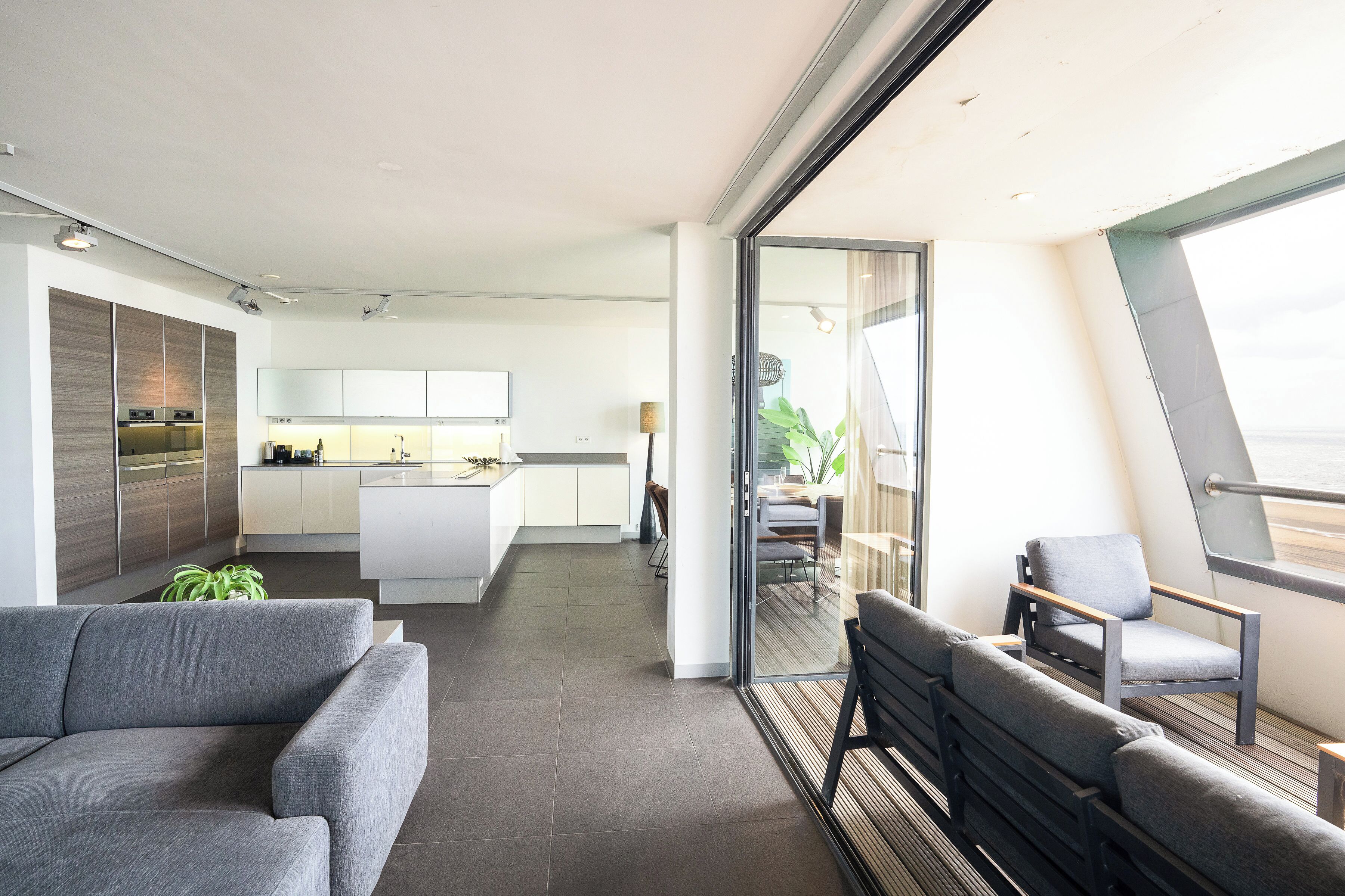 A modern interior with a sofa, chairs, a kitchen, and a balcony with a view.