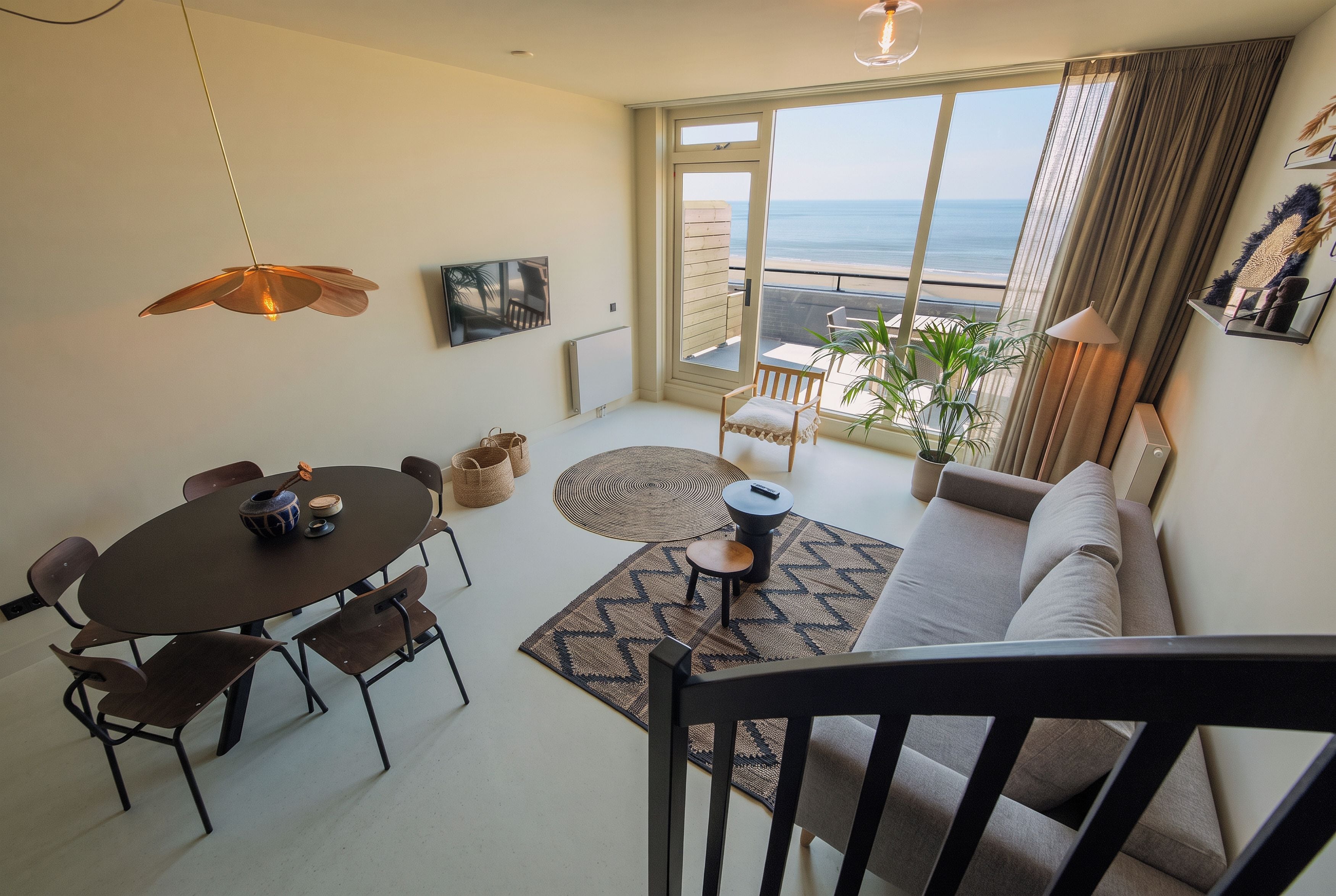 A modern living room with a dining area, a sofa, a coffee table, and a view of the sea through large windows.