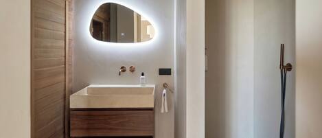 A modern bathroom with a wooden vanity, a round mirror, a handheld showerhead, and a towel rack.