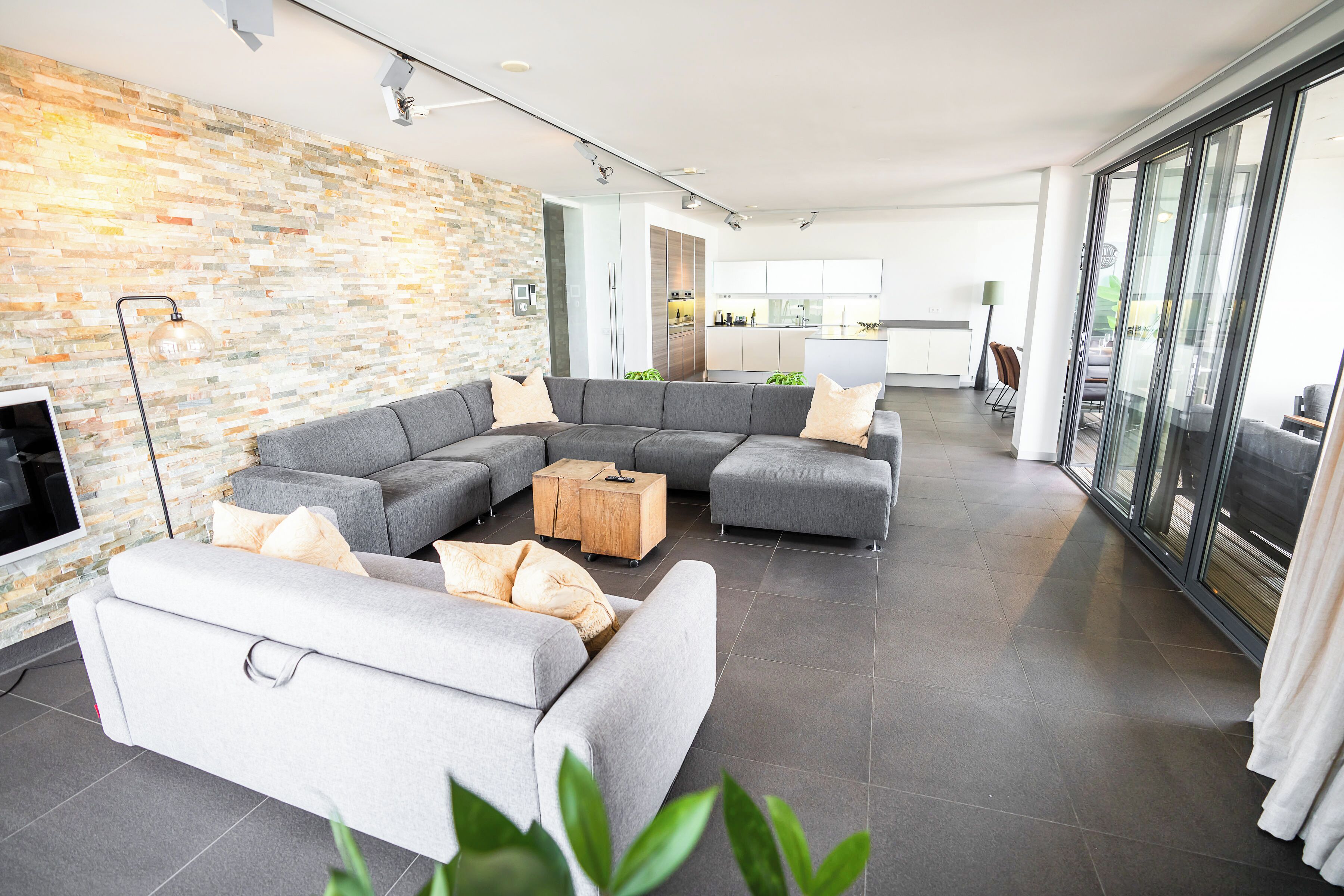 A modern living room with a sectional sofa, a wooden coffee table, and a stone-patterned wall.