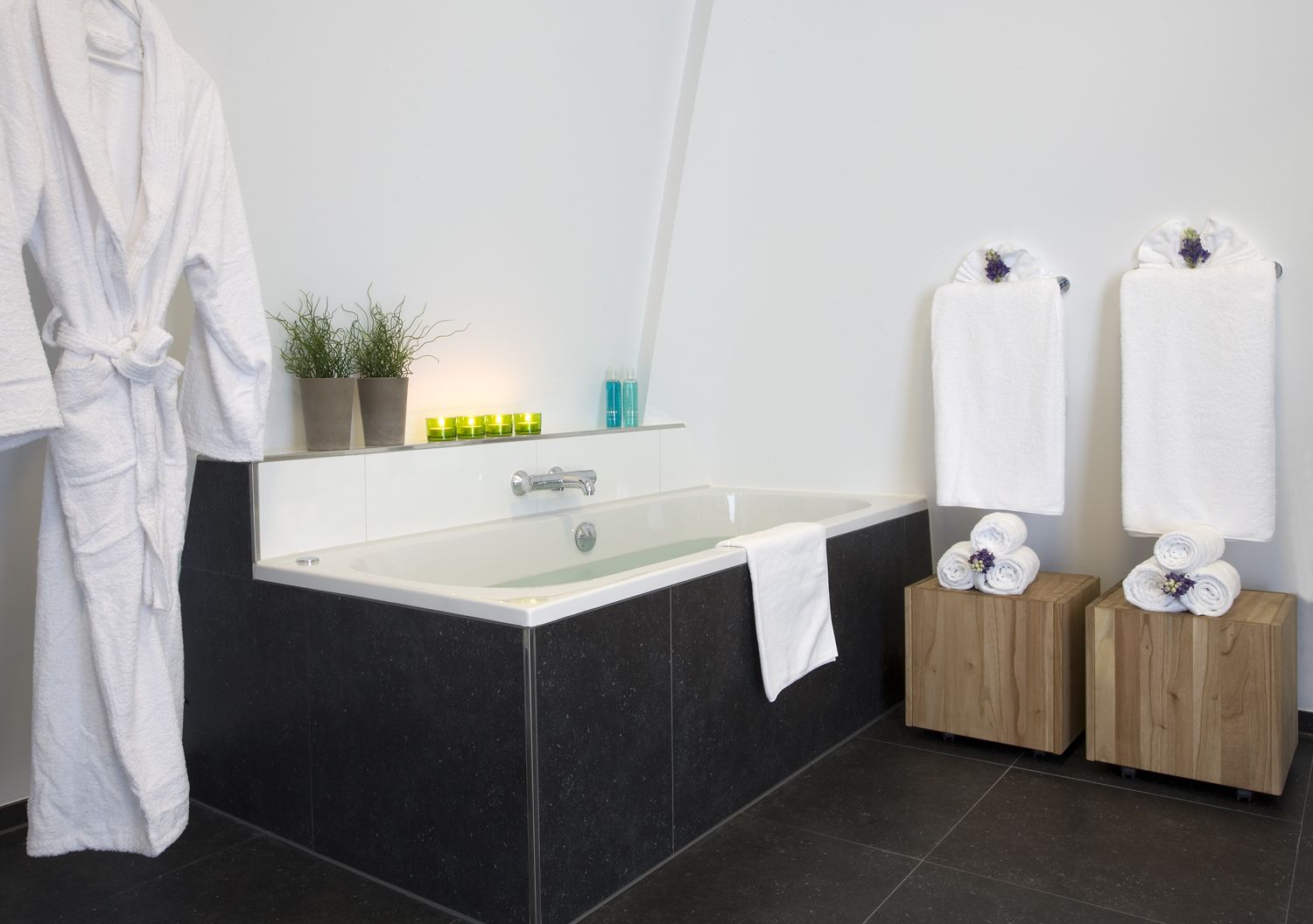 A modern bathroom with a bathtub, a white robe, and two wooden side tables with towels.