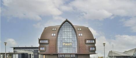 Un bâtiment moderne doté d’une grande façade arquée en verre et d’un toit brun, portant l’inscription « Poit ».