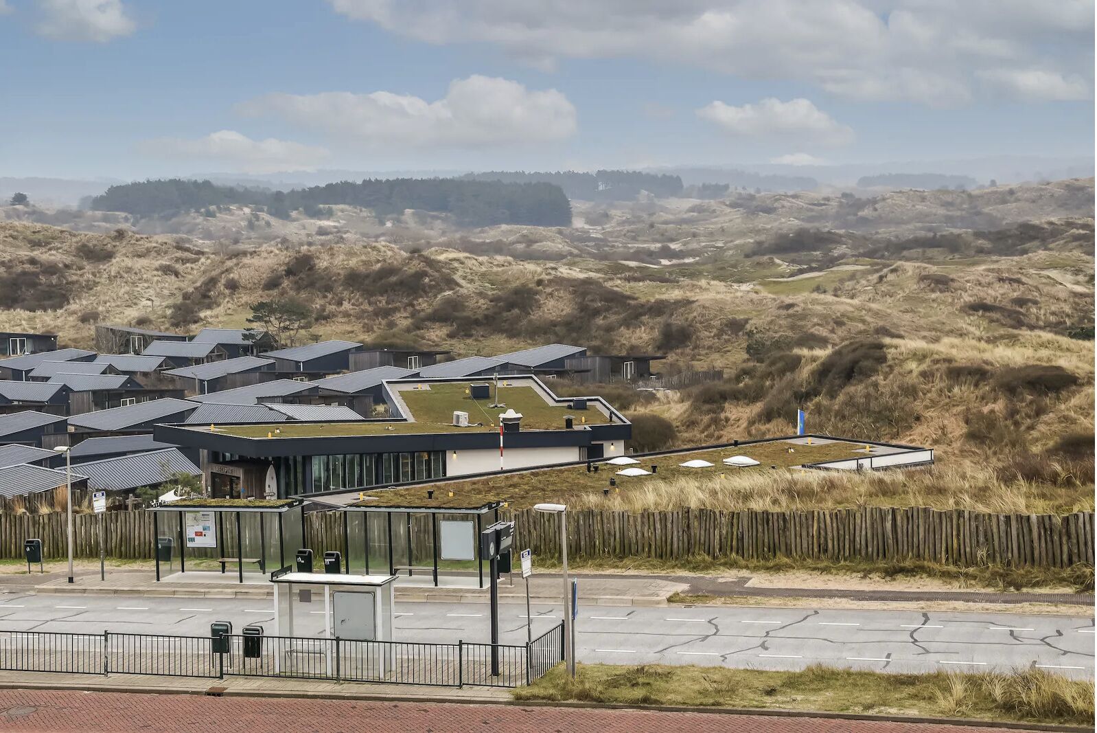 A modern building with multiple roofs, a parking area, and a view of the surrounding dunes.