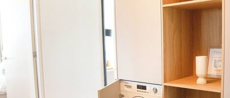 Une petite buanderie équipée d’un lave-linge Bosch, d’étagères en bois et d’une porte donnant sur une autre pièce.