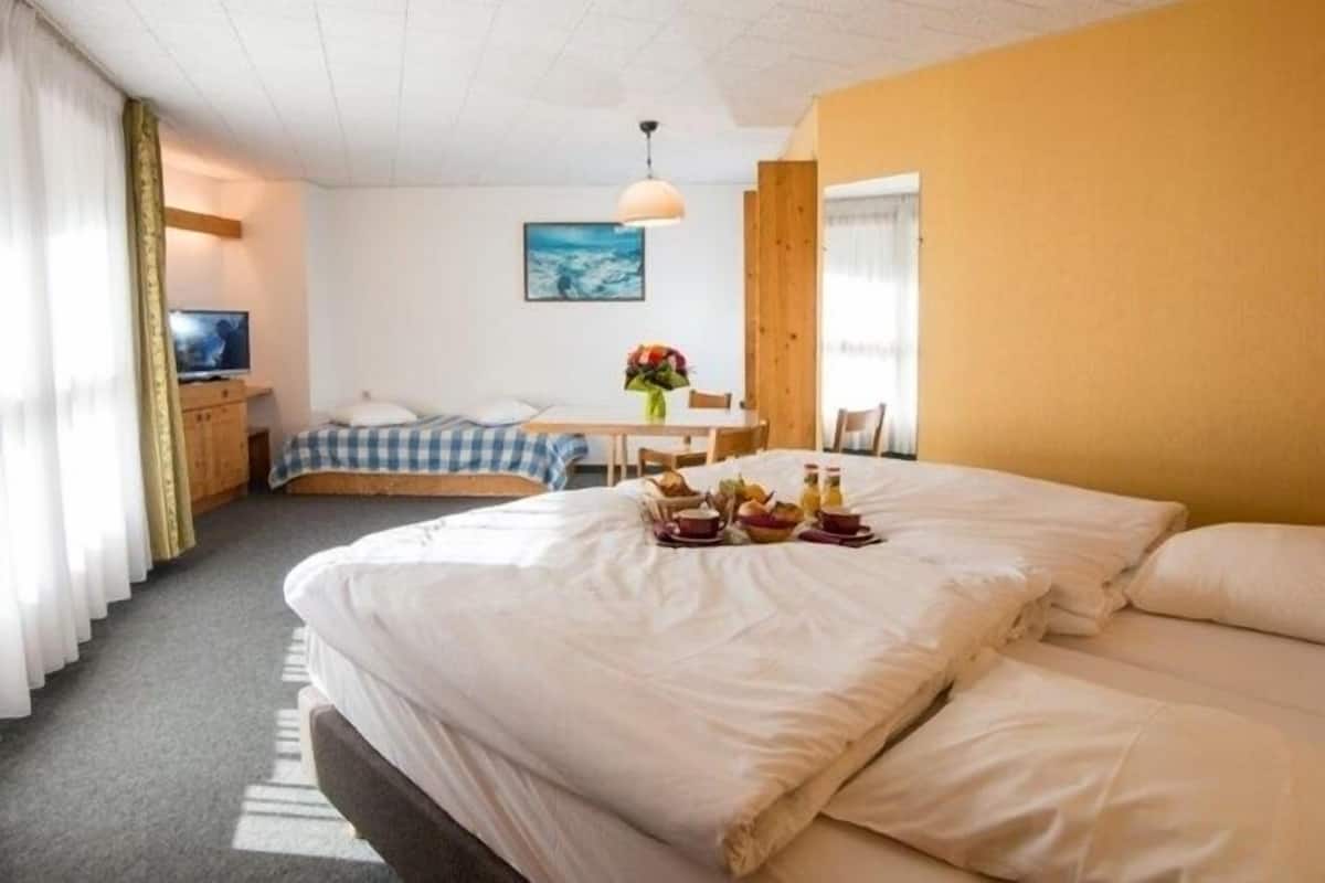 A hotel room with a large bed, a desk with a chair, a television, and a painting on the wall.