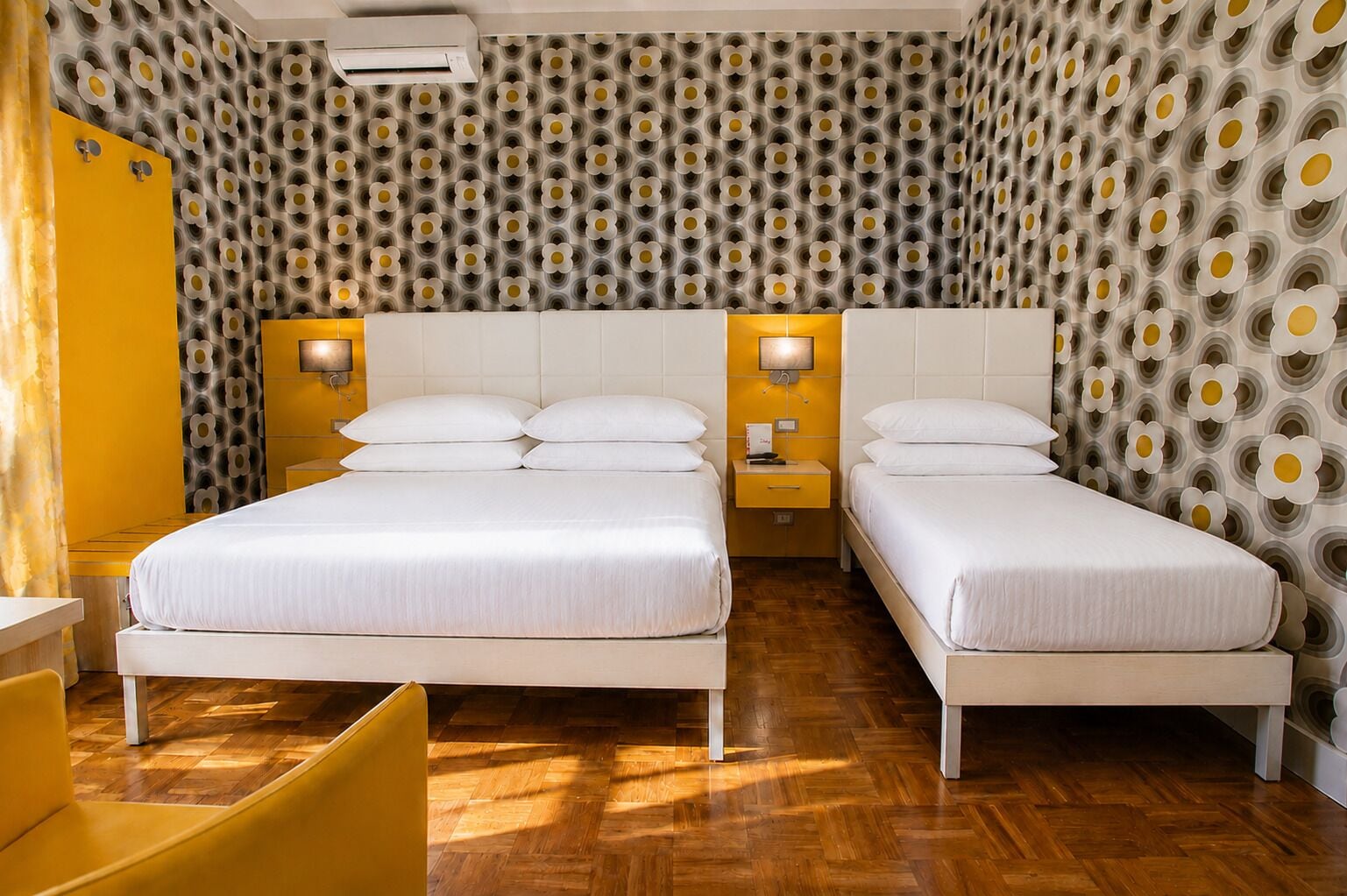 Habitación de hotel con dos camas, piso de madera y papel tapiz estampado.