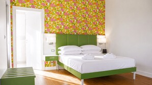 A hotel room with a green bed, white pillows, a nightstand, a lamp, and a small table with towels. - B&B Pellicano Guest House (Reggio Calabria)