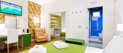 A hotel room with a bed, a desk with a chair, a television, and a bathroom visible through an open door.