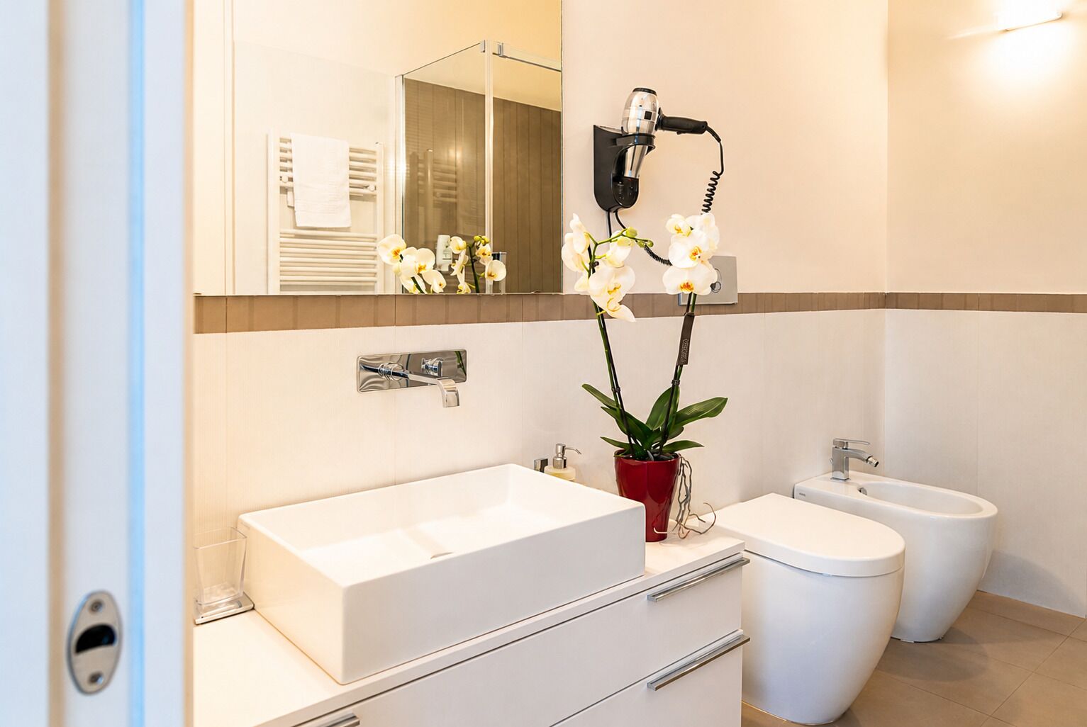 A modern bathroom with a white sink, a bidet, and a hairdryer mounted on the wall.
