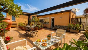 An outdoor patio area with a table set for breakfast, including croissants and fruit, and several lounge chairs. - B&B Pellicano Guest House (Reggio Calabria)