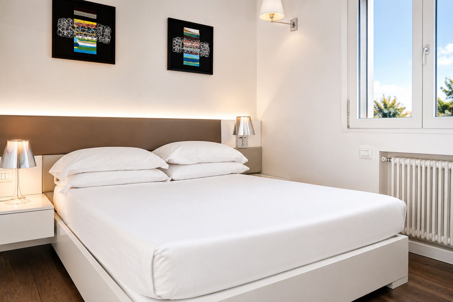 A hotel room with a bed, nightstands, wall-mounted lamps, and framed artwork.