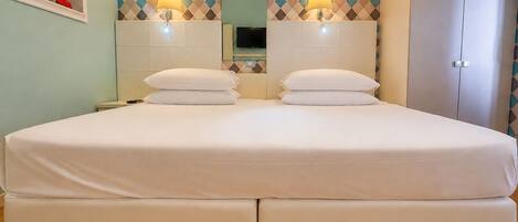A double bed with two pillows, a nightstand, a mirror, and two wall-mounted lamps.