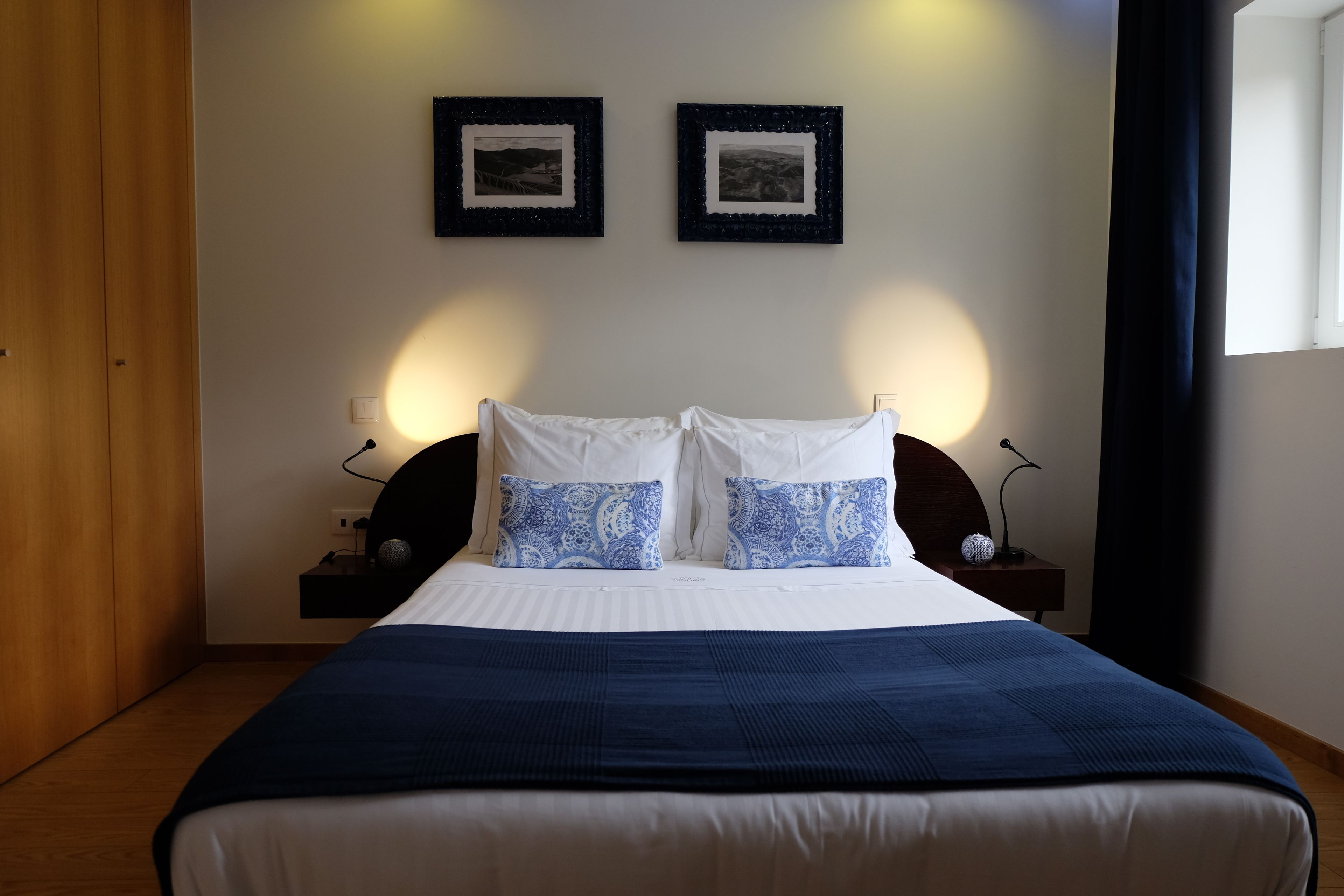 A neatly made bed with a blue blanket, two bedside tables with lamps, and two framed pictures on the wall.