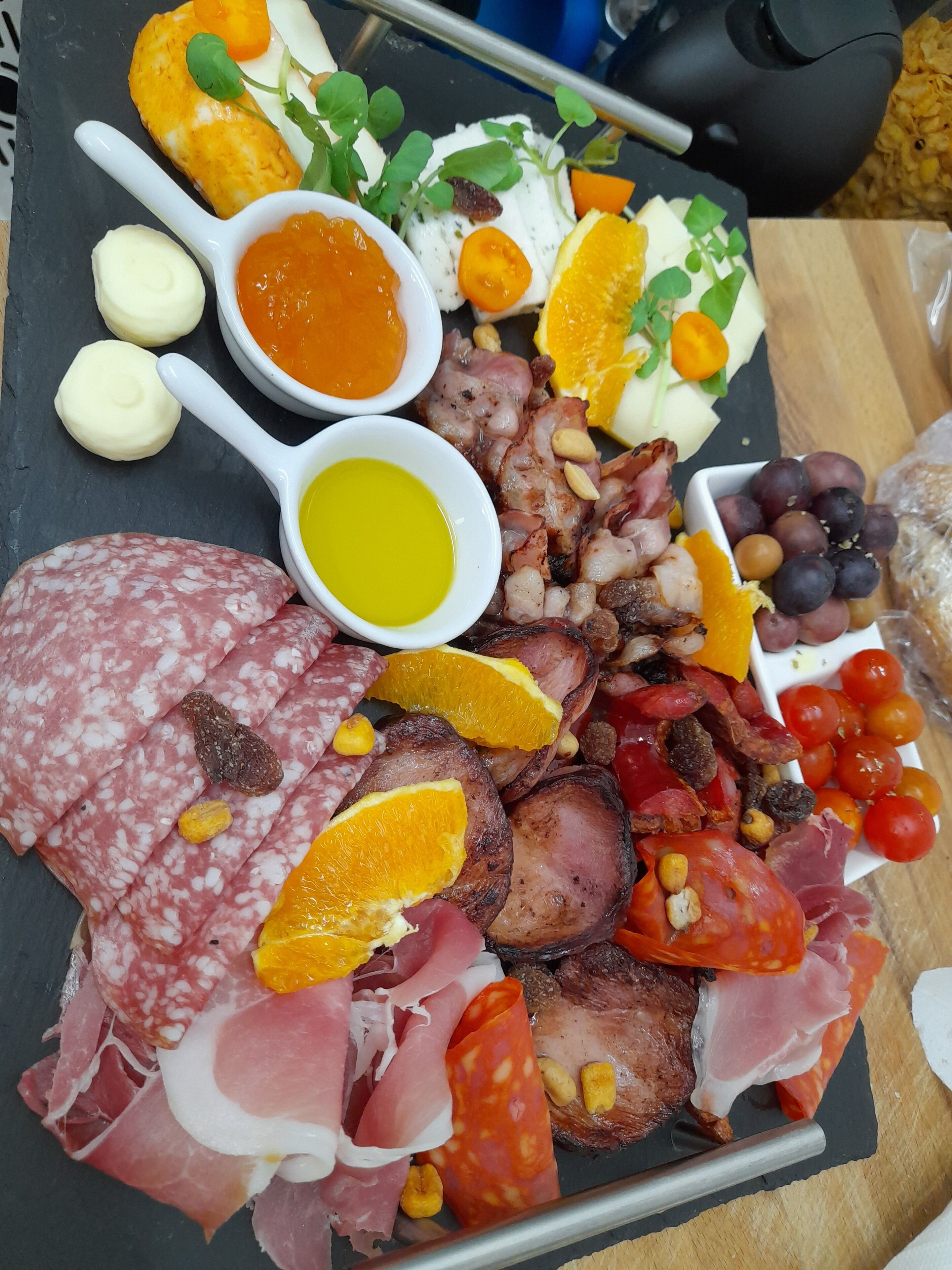 Una tabla de embutidos con diversos tipos de carne, quesos, frutas y salsas.