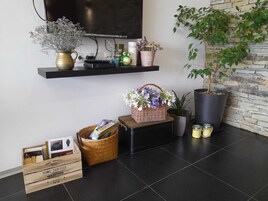 Una sala moderna con un televisor de pantalla plana montado en la pared, una pared de piedra, una planta en maceta, un estante con objetos decorativos, un cesto de flores y un caja de madera con libros.