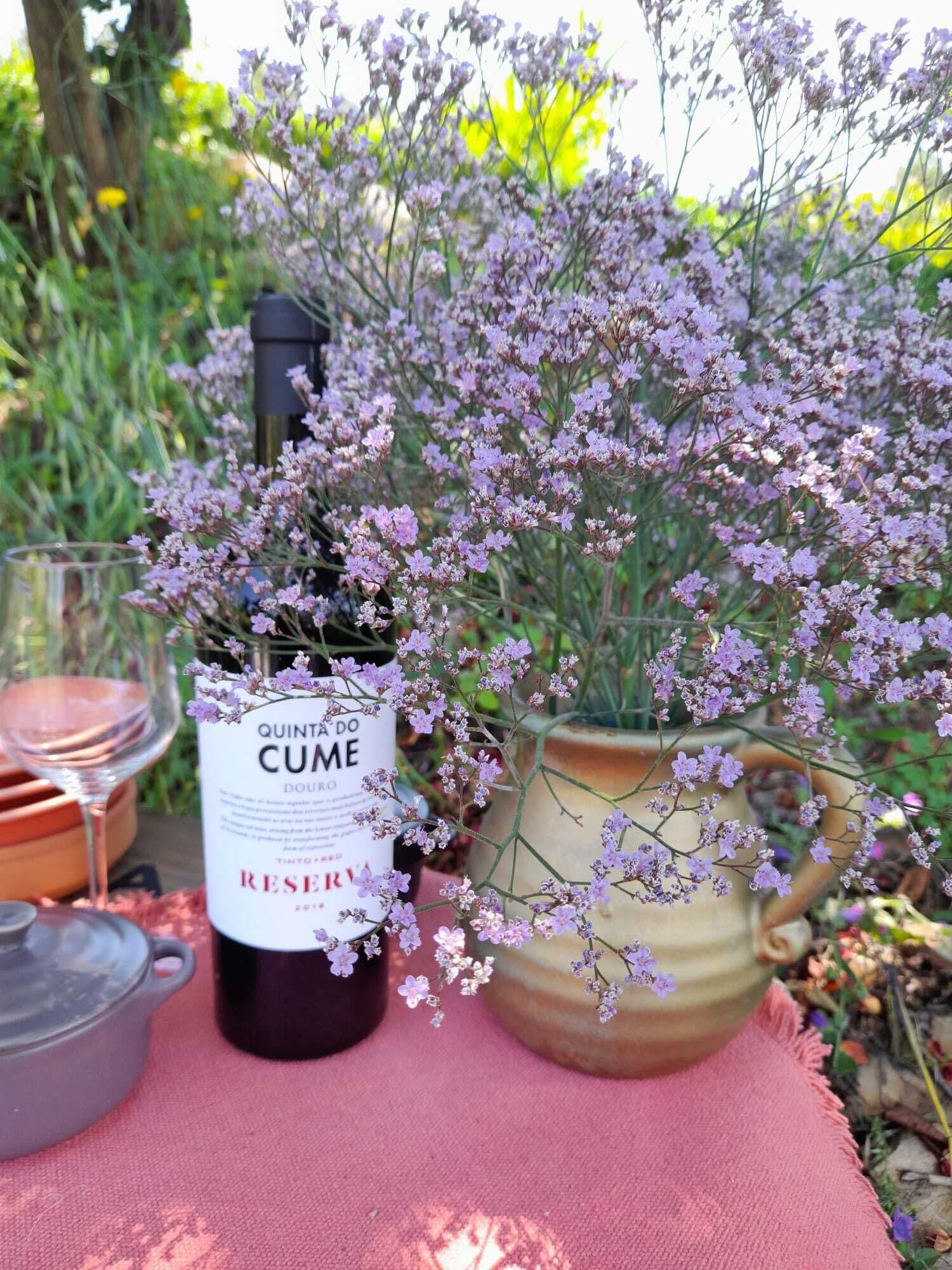 A bottle of wine, a glass, and a potted plant with purple flowers on a table.