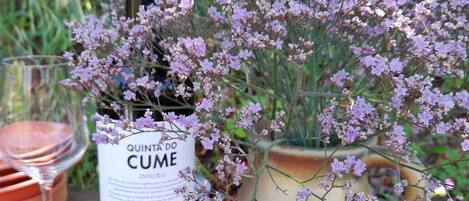 A bottle of wine, a glass, and a potted plant with purple flowers on a table.