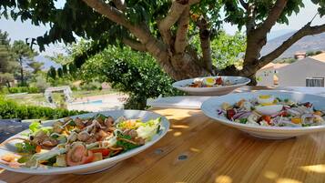 A table with three plates of salad under a tree, overlooking a pool and greenery.