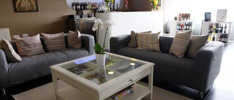 A modern living room with two grey sofas, a white coffee table, and a bar area in the background.