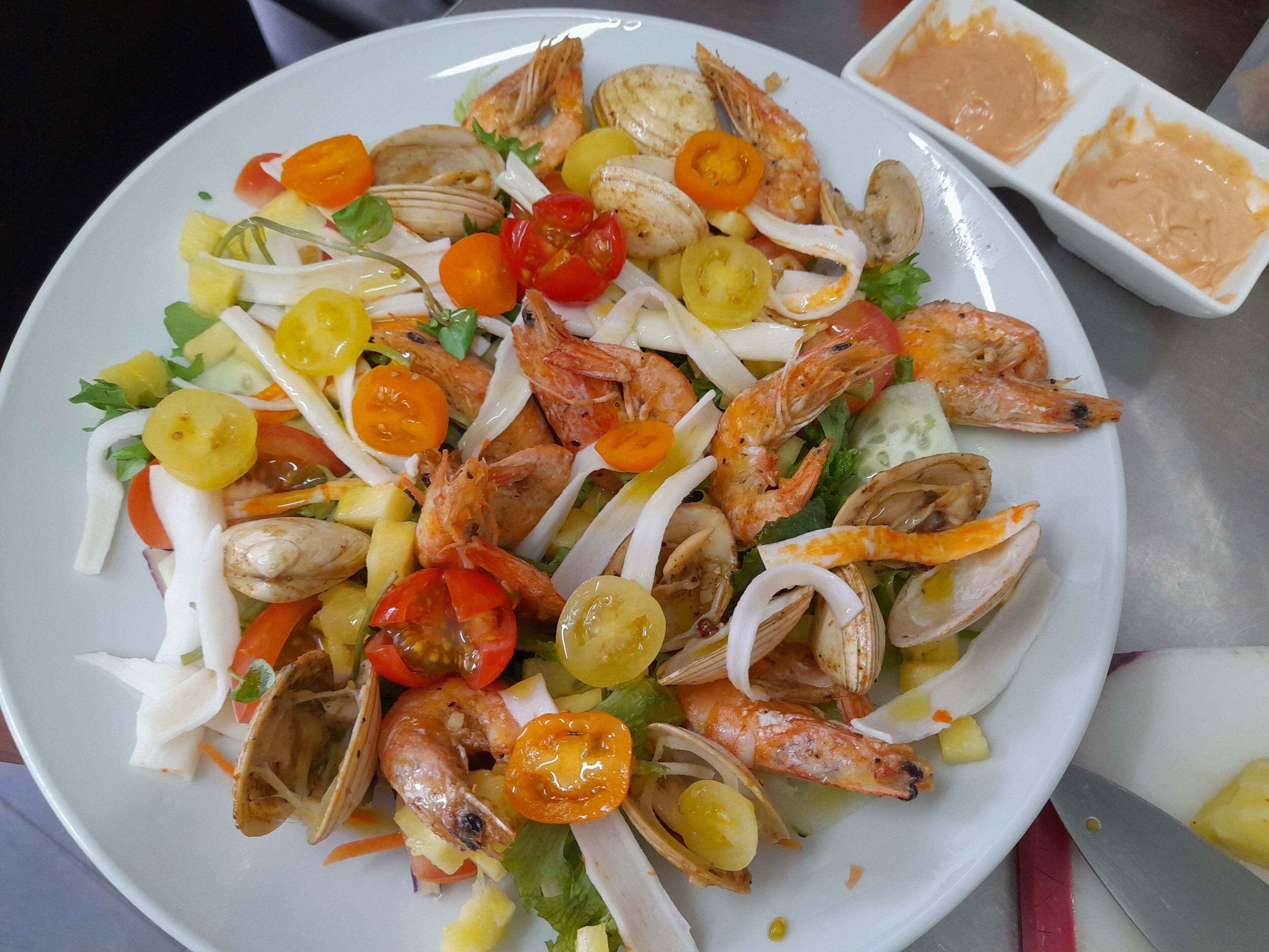 Ein Teller mit Meeresfrüchtesalat, darunter Garnelen, Muscheln und Kirschtomaten.