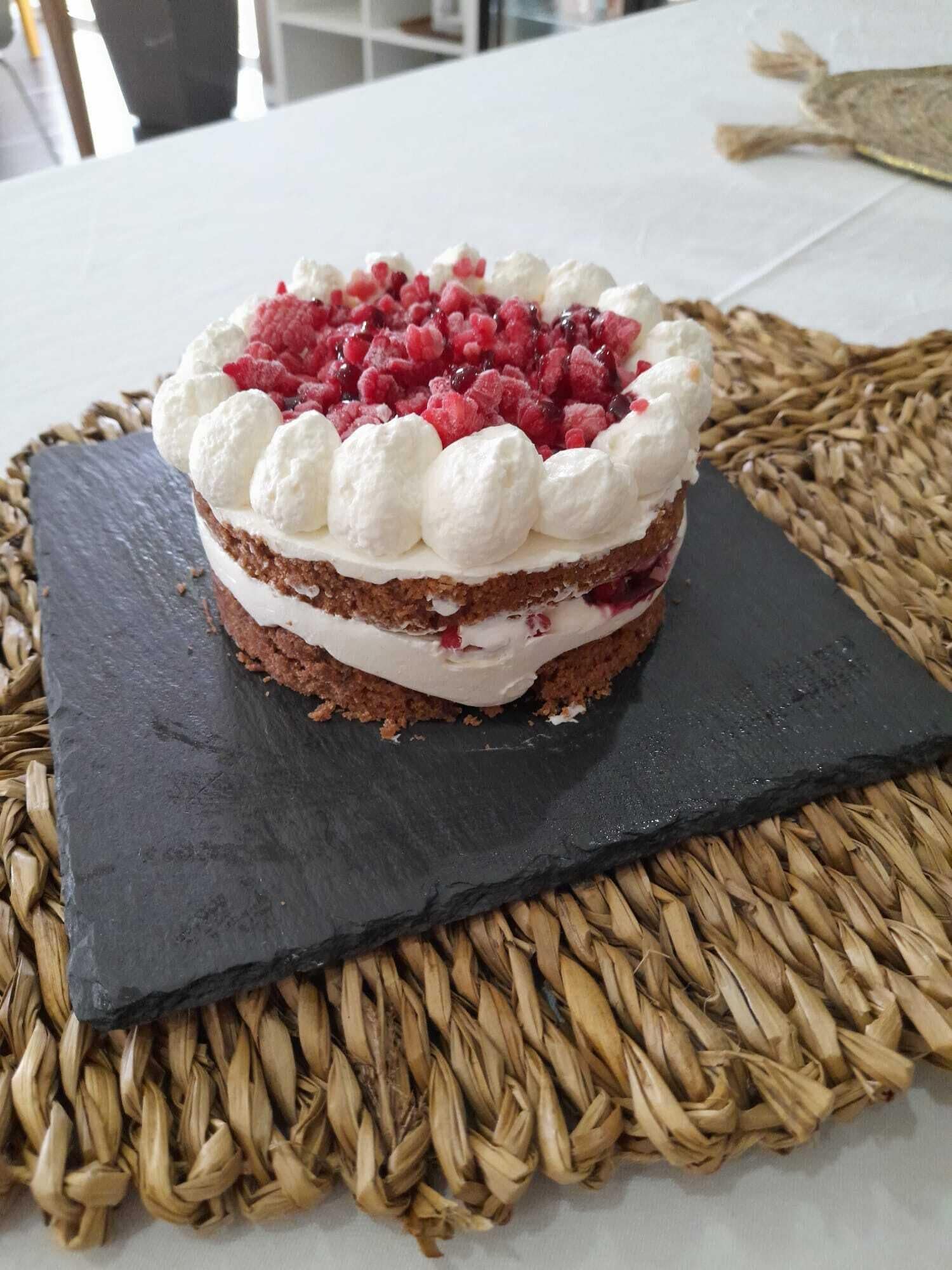 A layered dessert cake with white frosting and red fruit on a black slate.