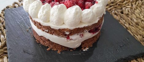 Un pastelito de varios niveles con glaseado blanco y fruta roja sobre una losa negra.